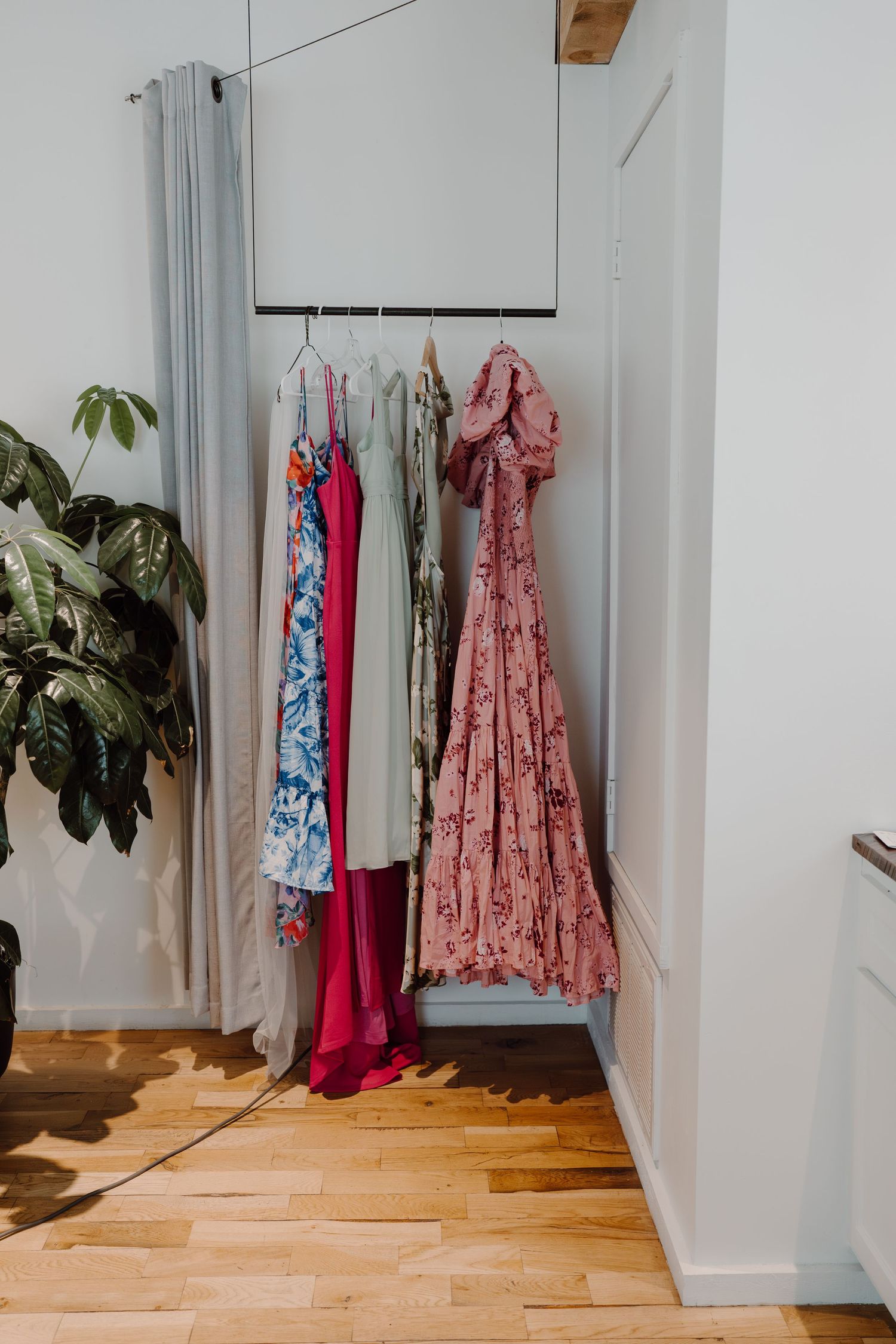 Colorful dresses hanging in a bright hallway with hardwood floors and white walls.