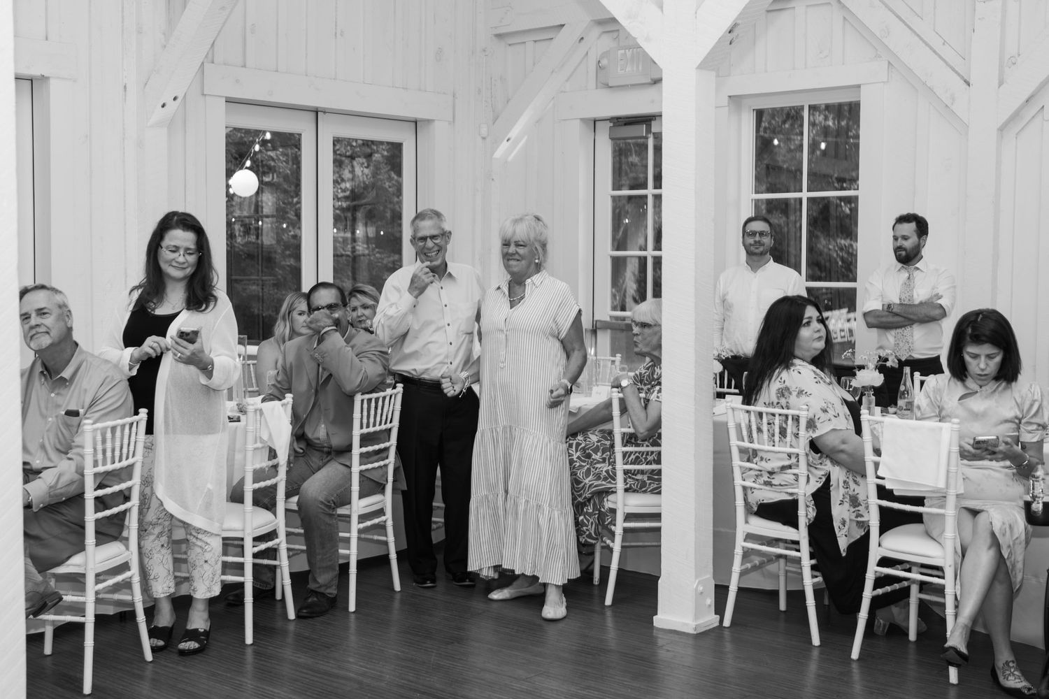 Wedding guests seated at tables along the wall of a bright white reception venue.