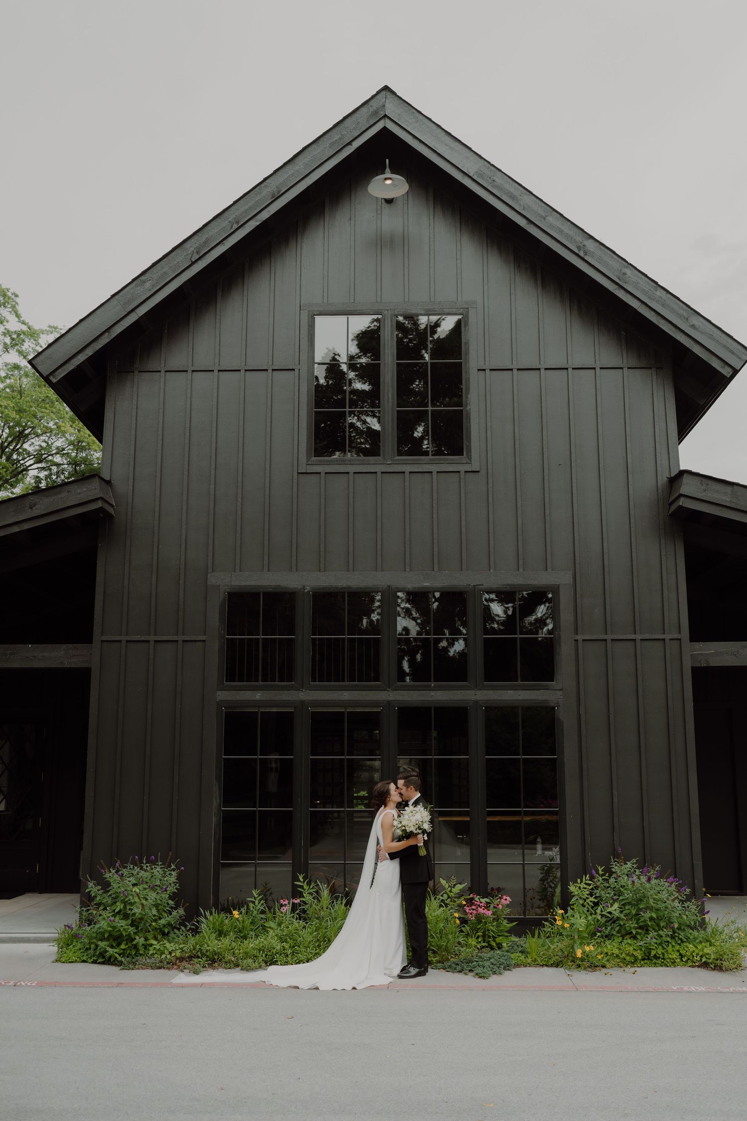 Modern black barn-style wedding venue with large windows and landscaped garden.