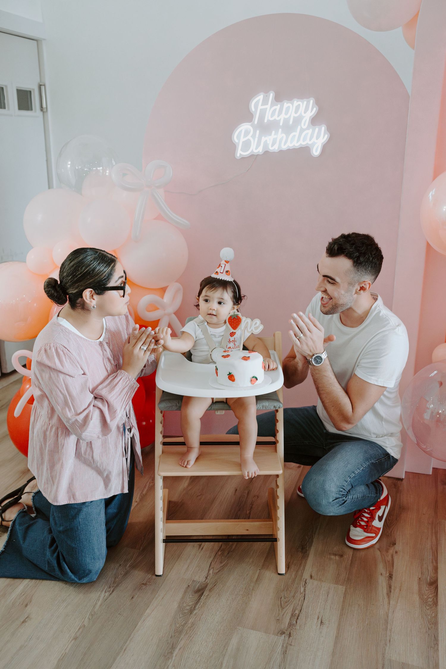 Birthday party setting with pink balloon arch and illuminated happy birthday sign.