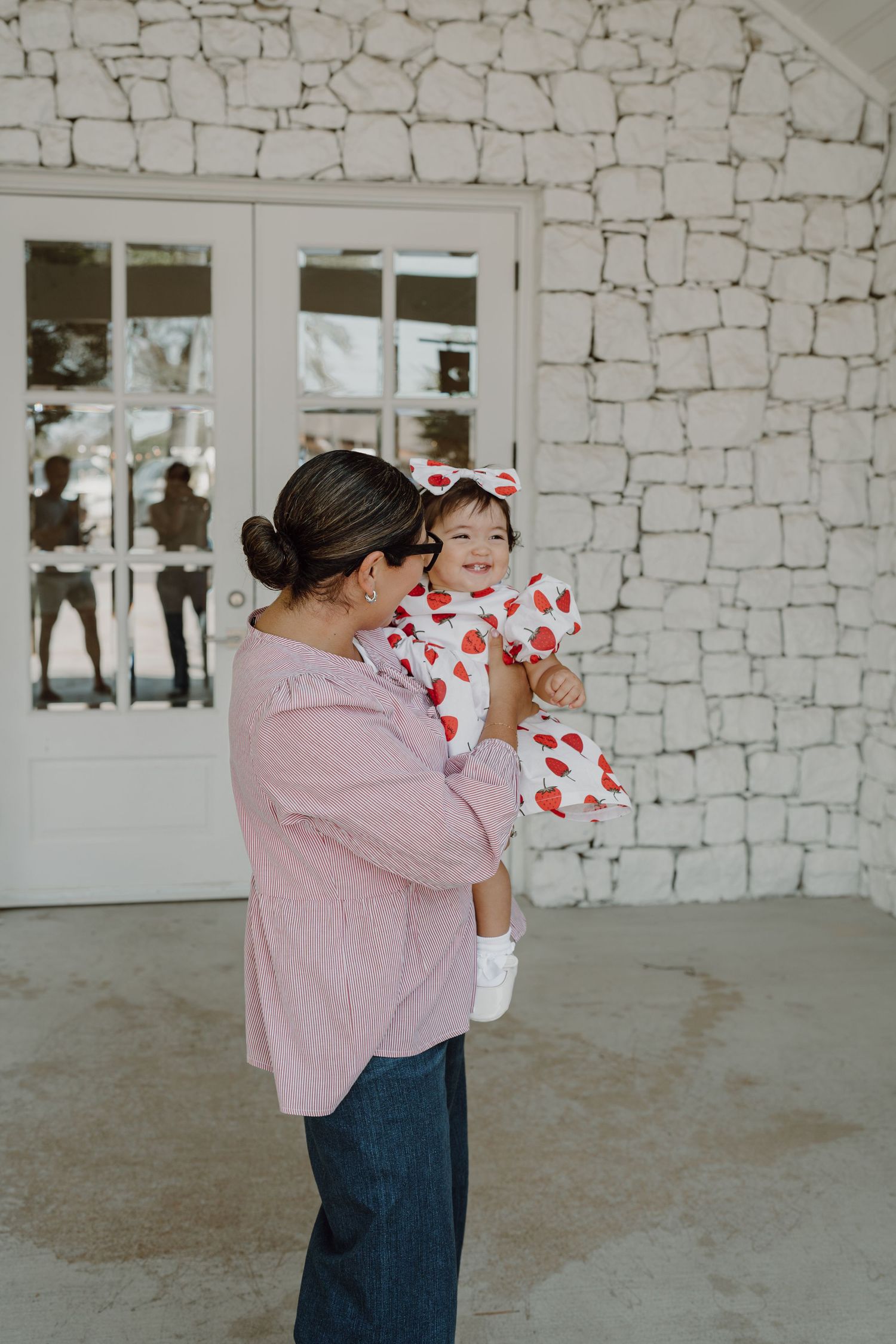 Parent and child share tender moment in coordinated outfits by white stone wall.