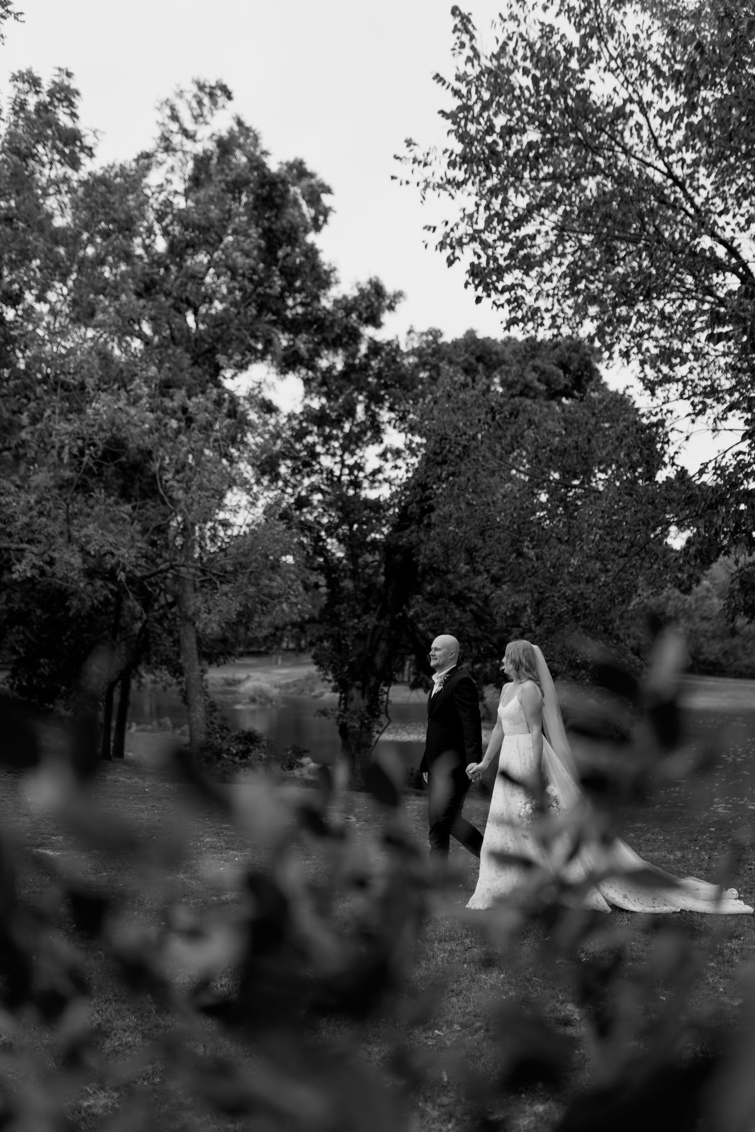 Black and white wedding photo showing a couple walking through a wooded landscape.