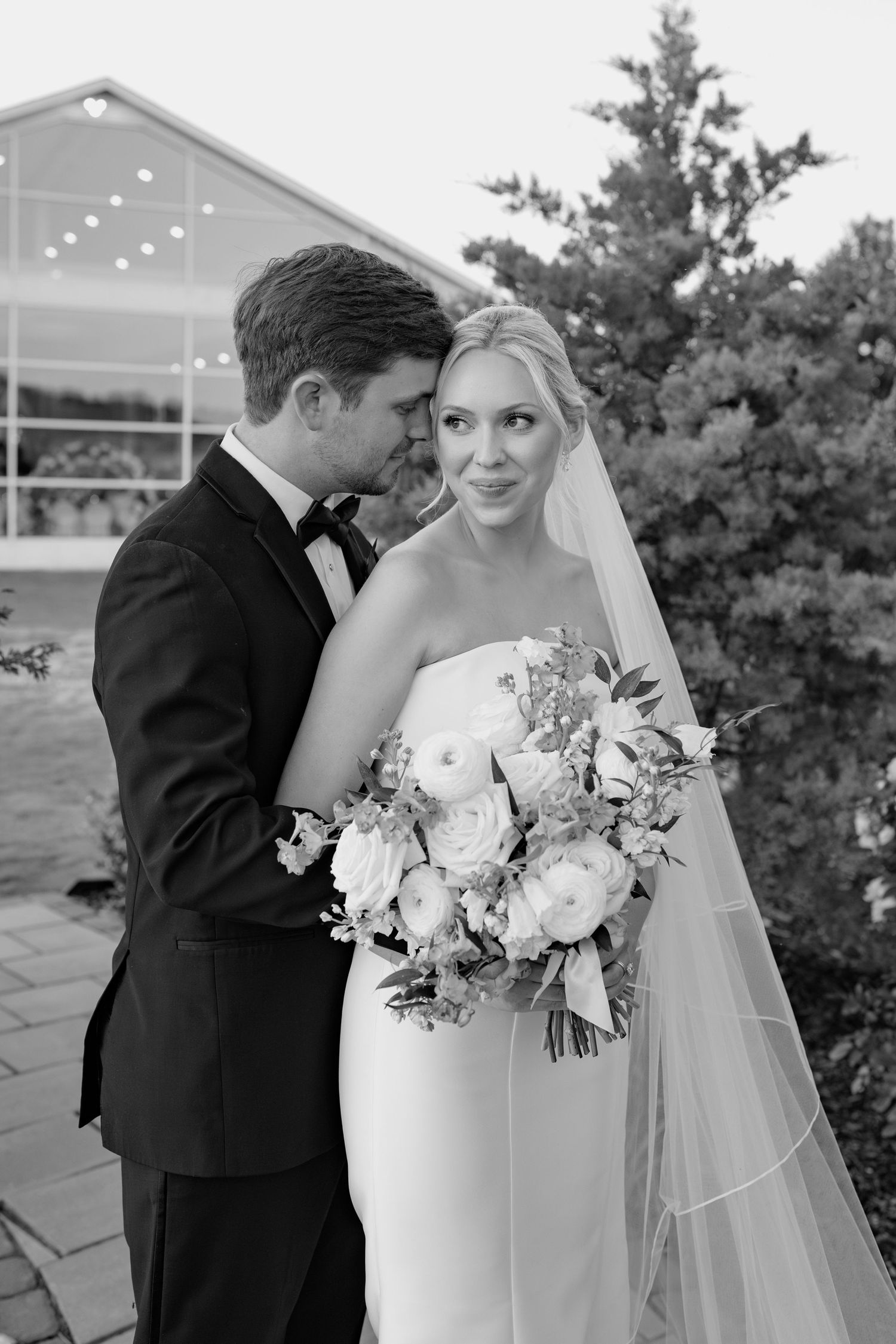 Elegant wedding portrait in front of a venue with string lights and greenery.