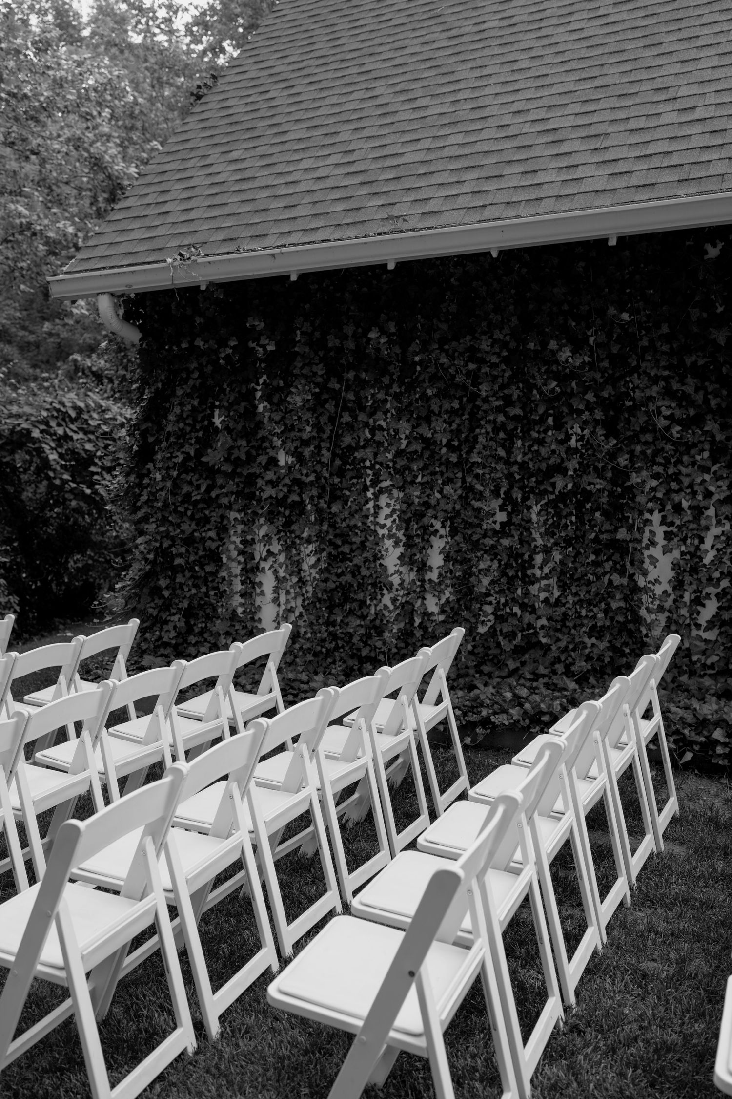 White folding chairs arranged in rows for an outdoor ceremony under a shingled roof.