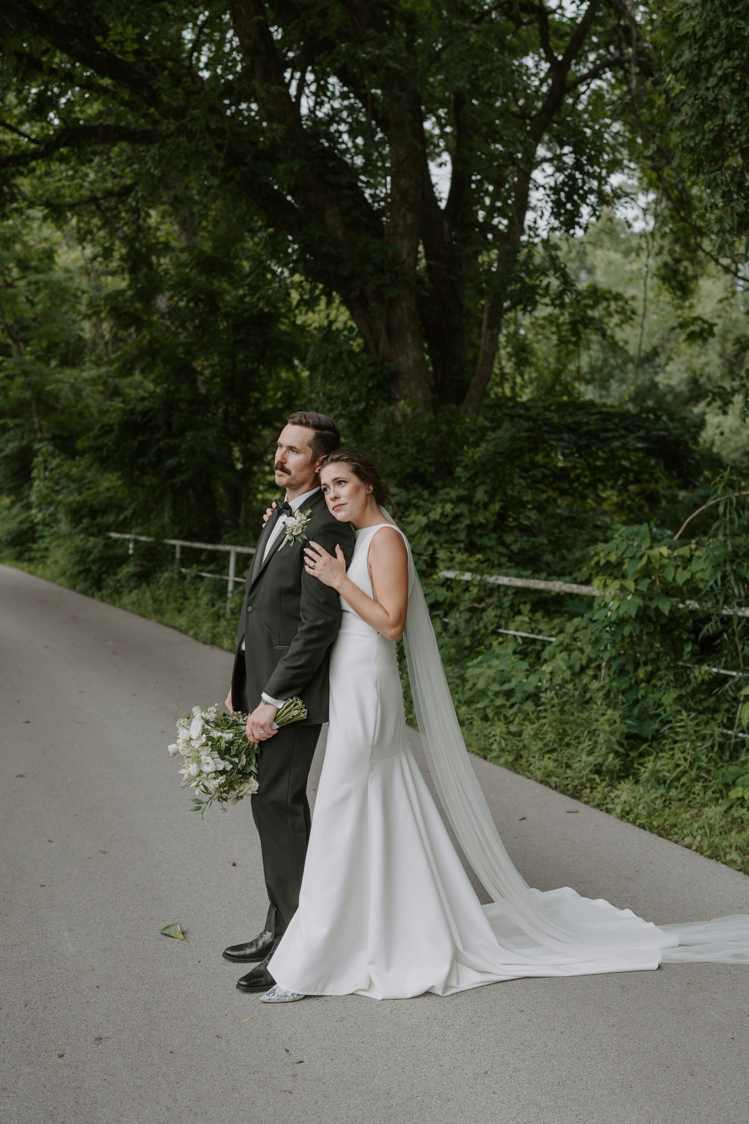 Artistic wedding photo capturing a couple on a serene forest path with flowing white dress and veil.