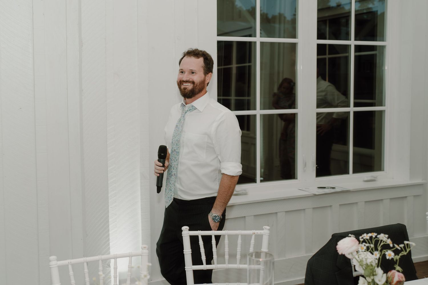 Wedding guests gather and chat in a modern white reception space with windows.