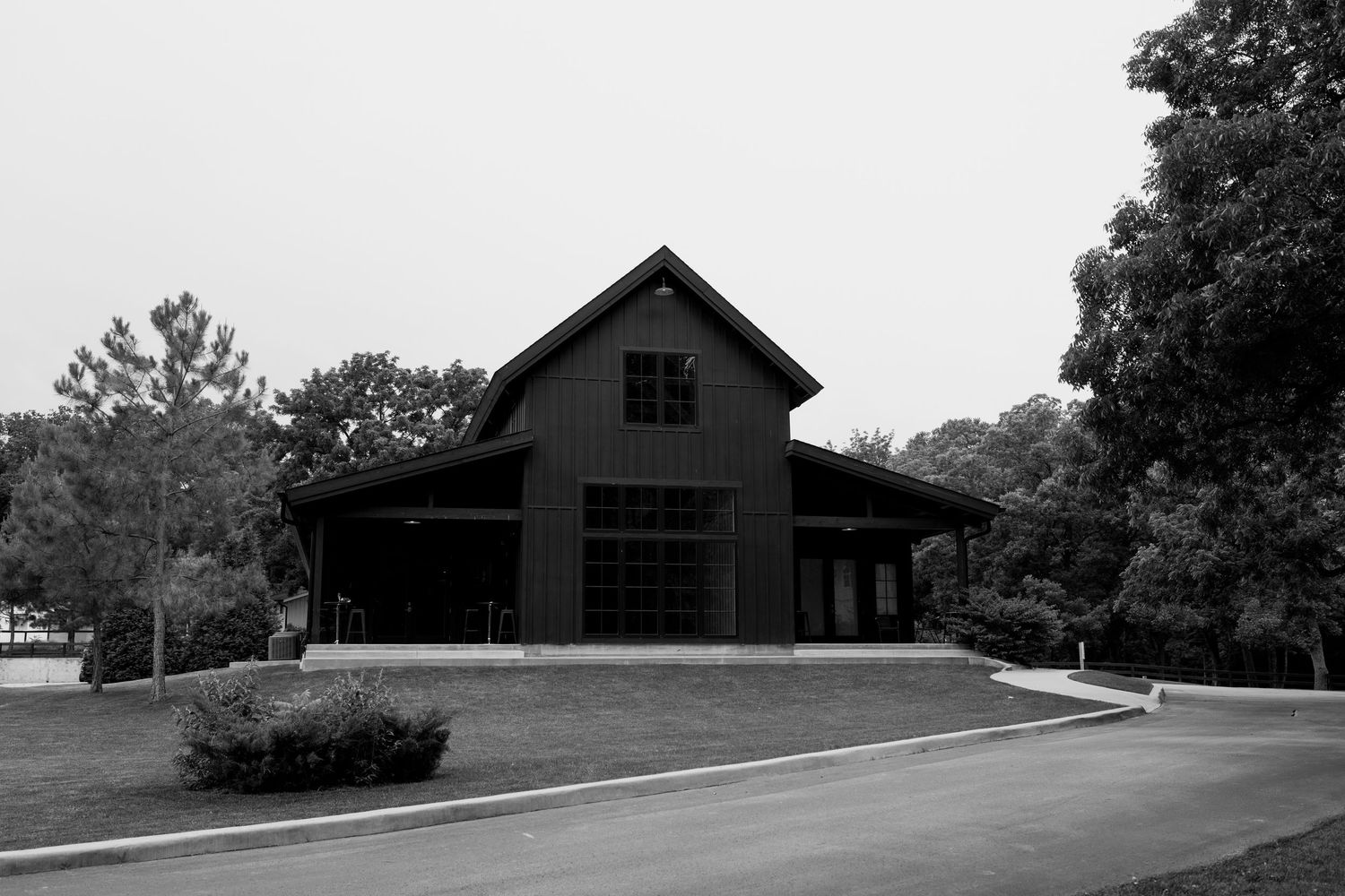 Panoramic view of a dark barn building nestled on a hillside surrounded by trees.