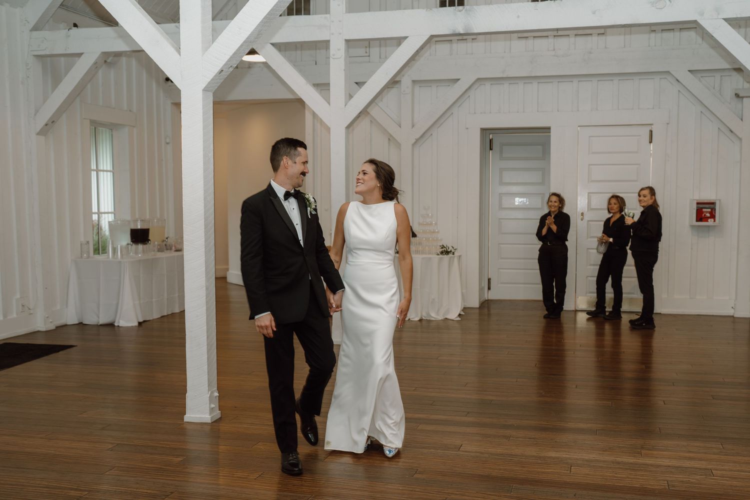 Wedding couple dancing in an elegant white barn venue with hardwood floors and exposed beams.