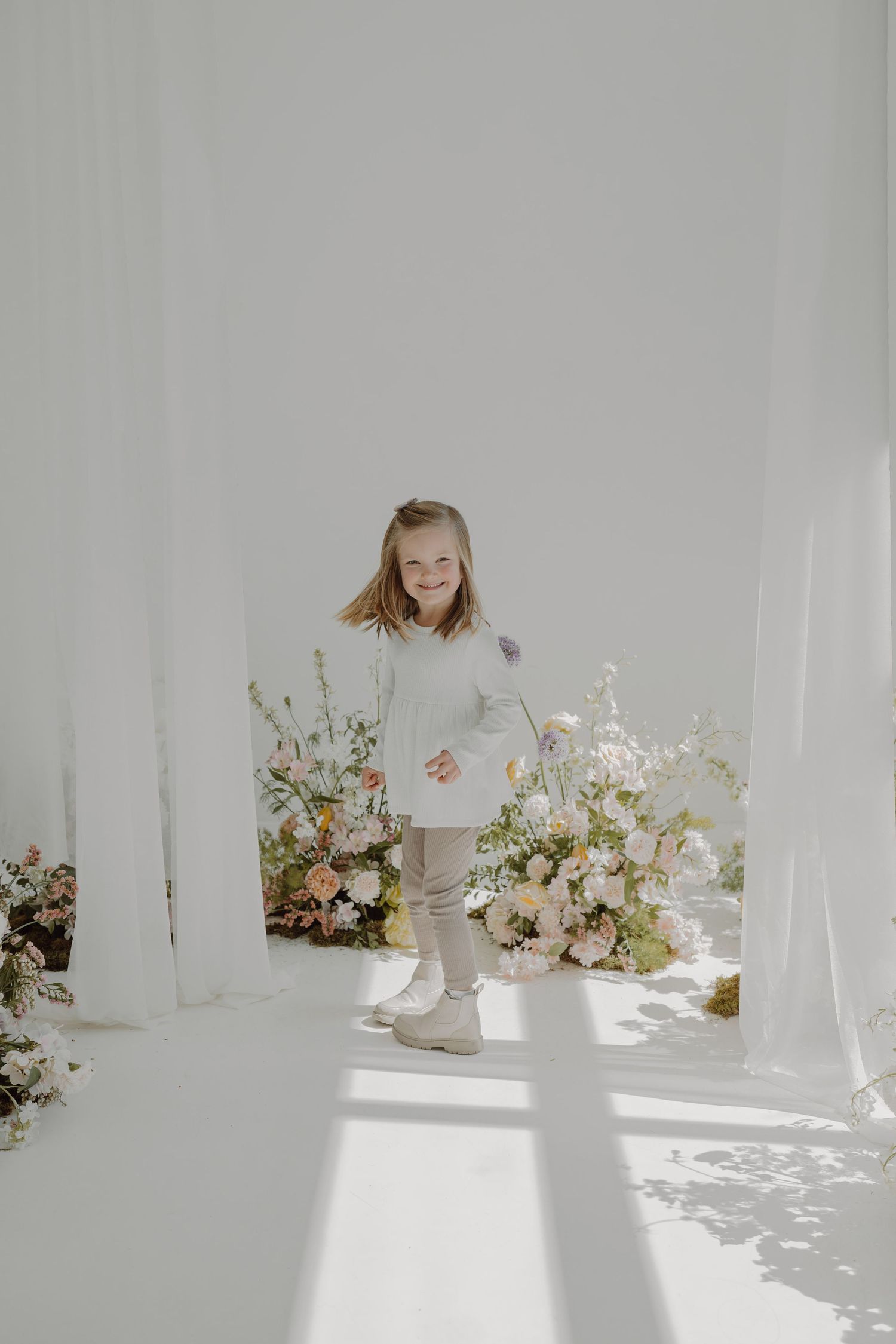 Minimalist white studio with scattered floral arrangements and decorative ceramic pieces.