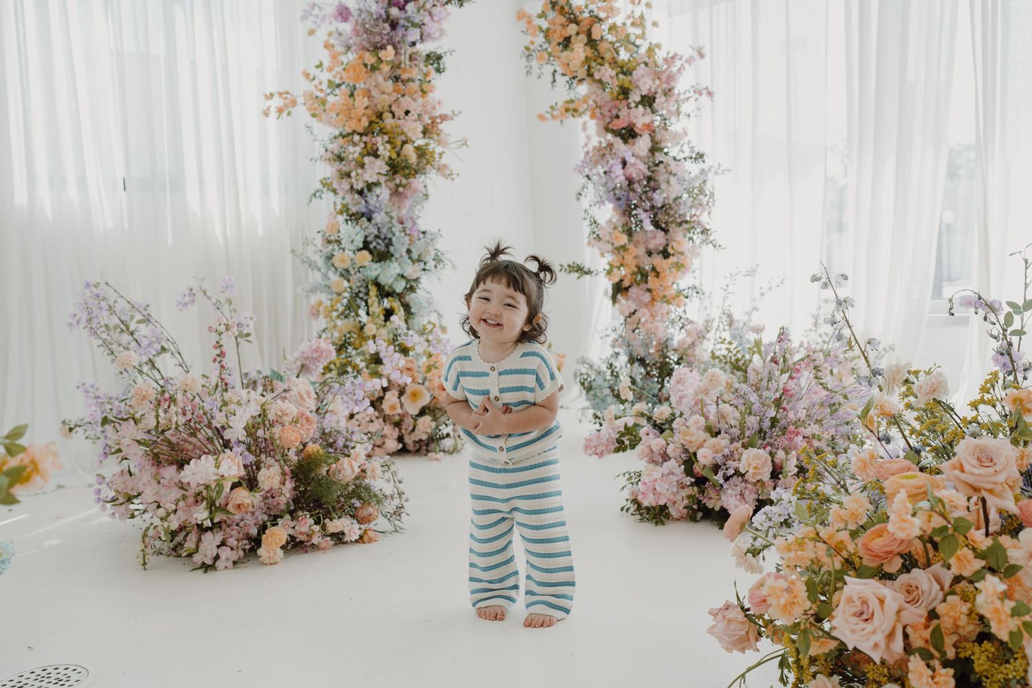 Elegant floral arrangements frame a white studio space with soft pink and peach blooms.