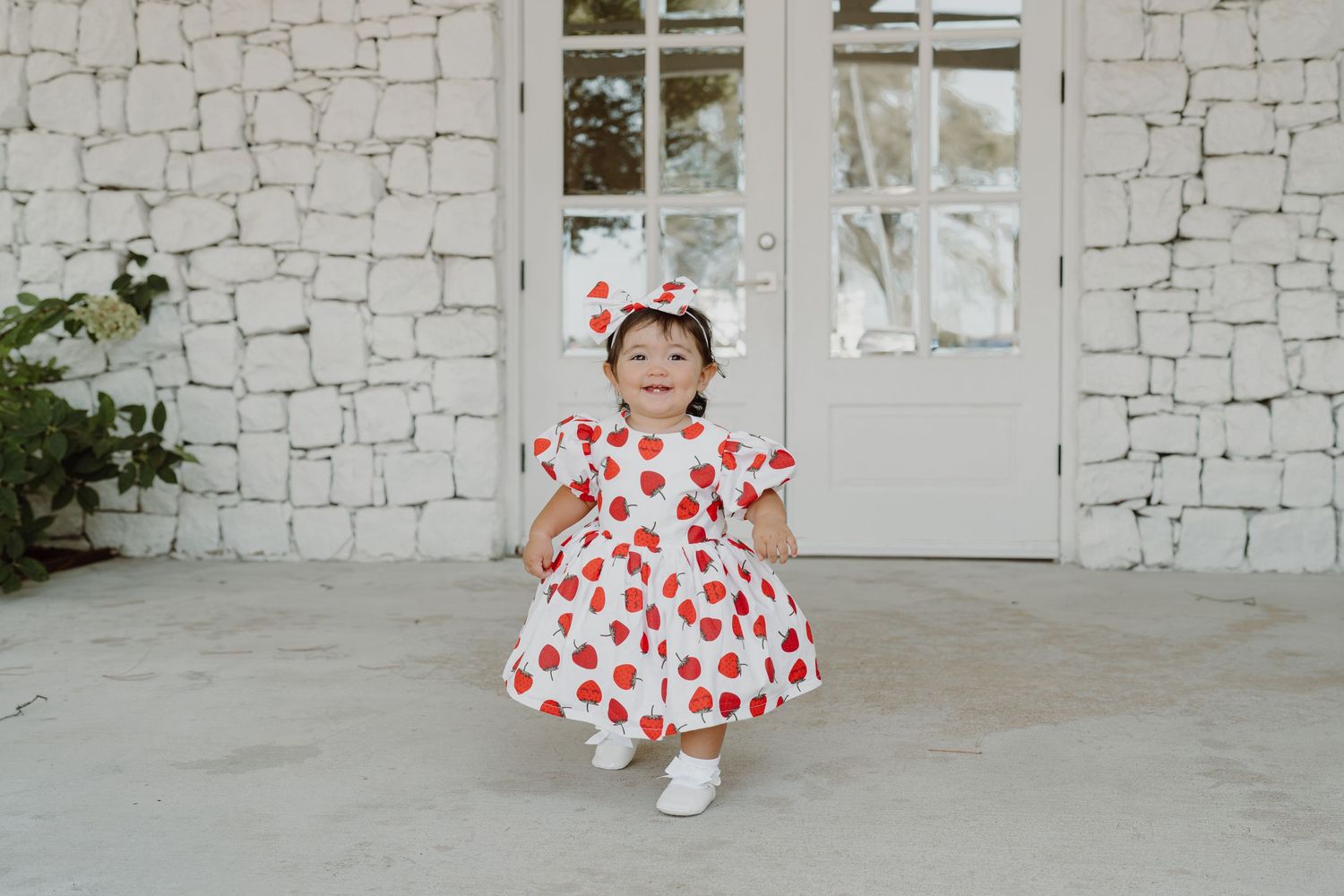 Joyful moment captured in heart-print dress and bow against white stone wall.