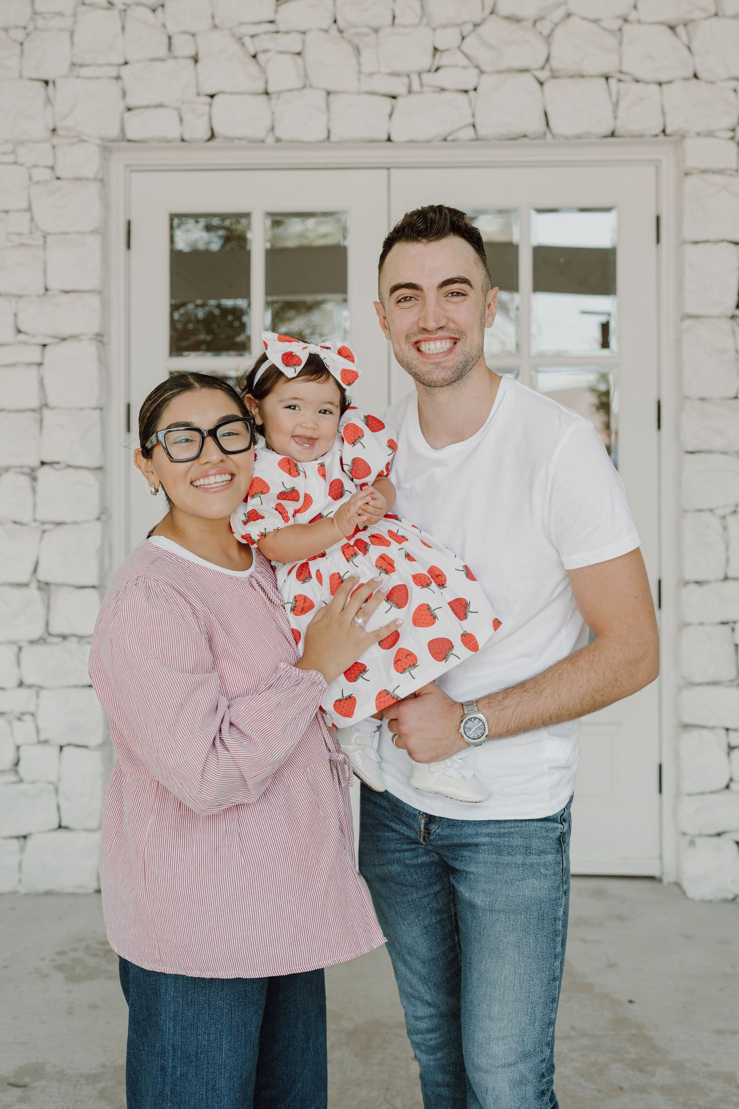 Family photoshoot against white brick wall with heart-patterned dress and casual attire.