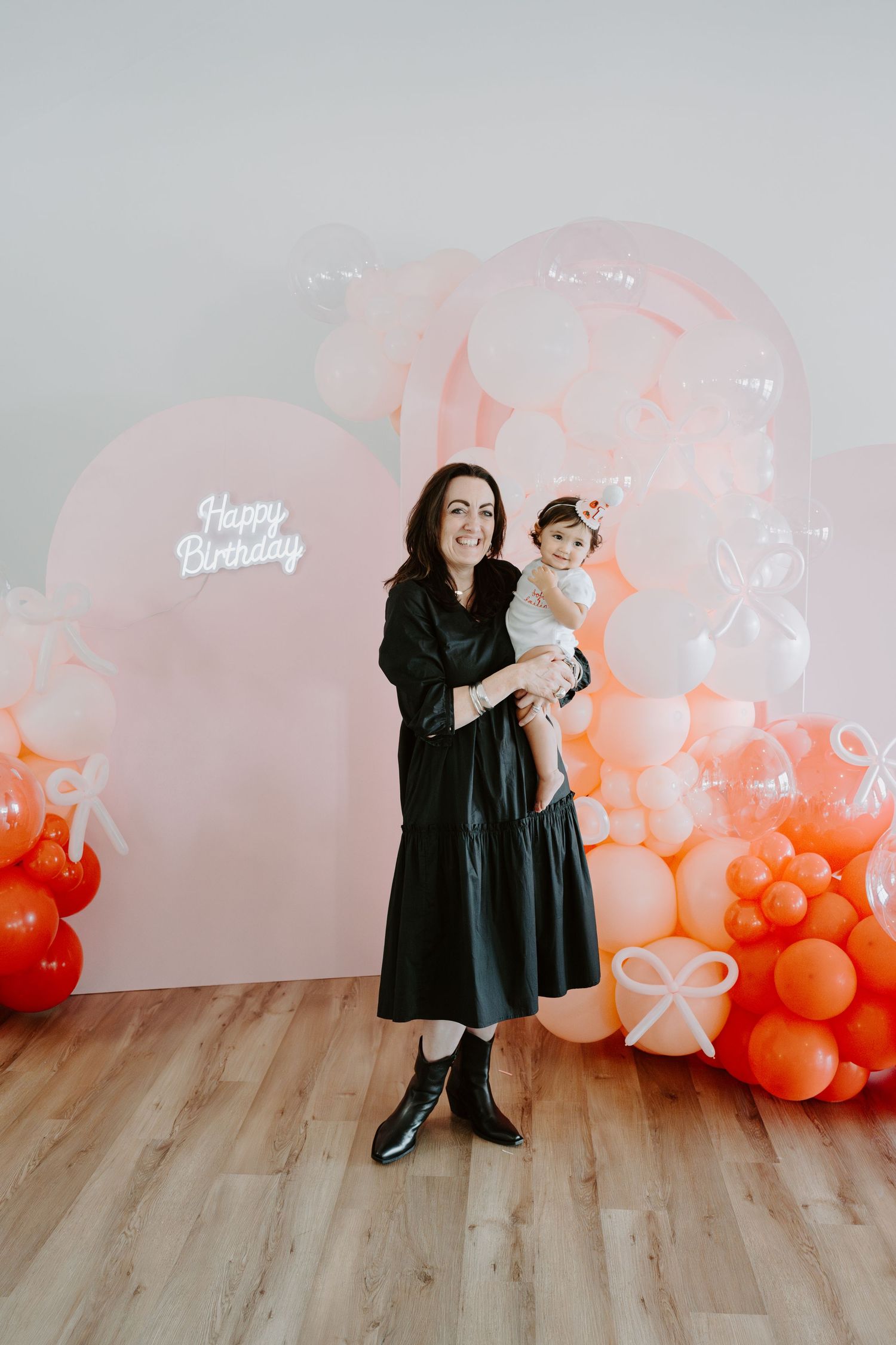 Modern birthday photo setup with coral balloon garland and 'Happy Birthday' text on wall.