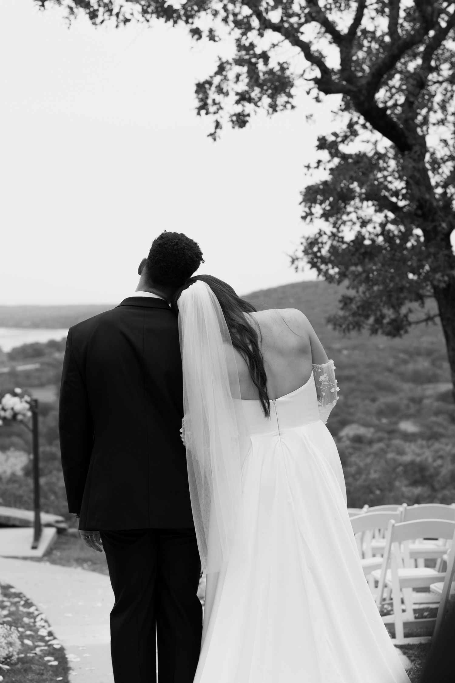 A wedding couple walks along a scenic overlook with rows of white chairs and autumn trees.