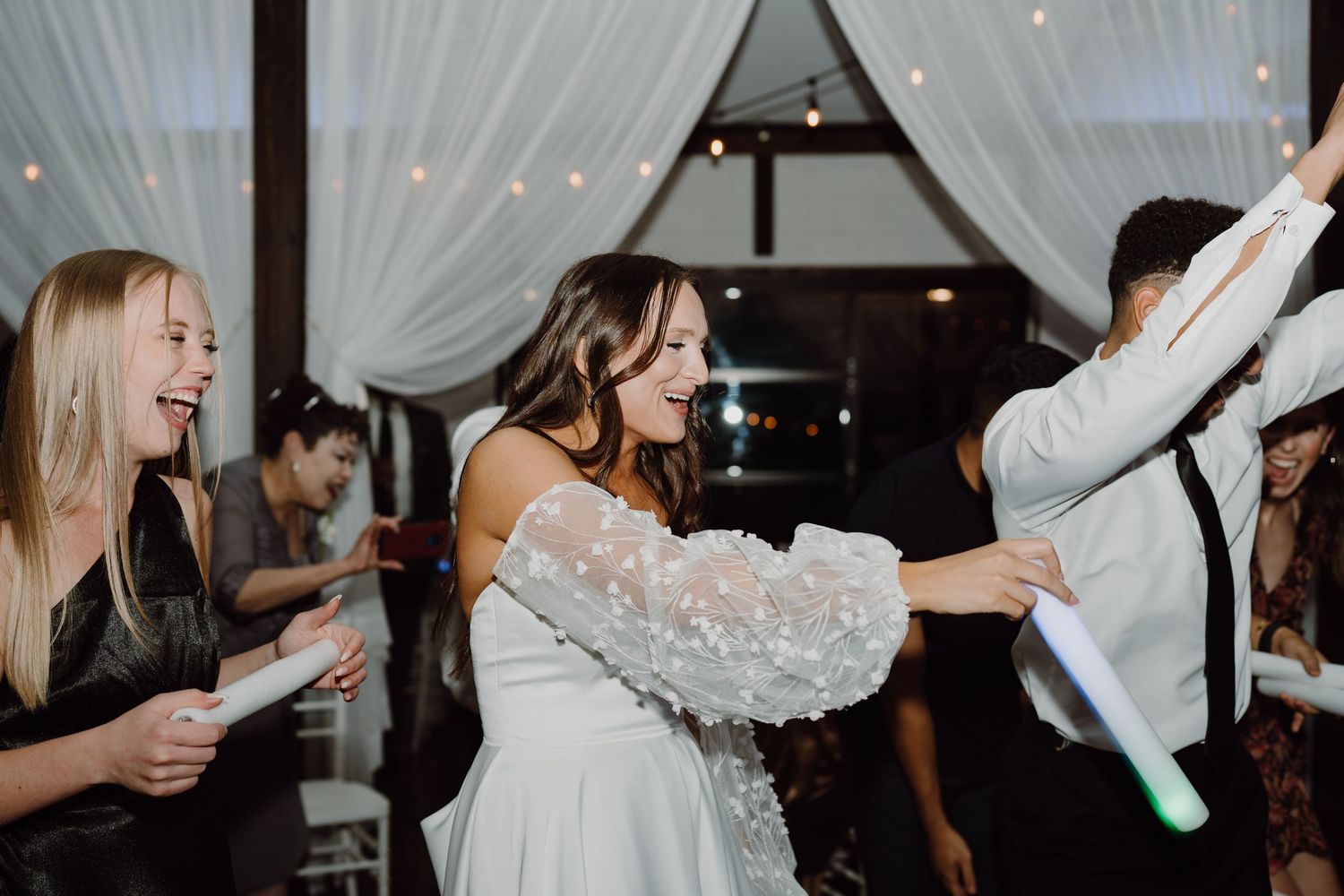 Guests enjoying a lively celebration under white fabric draping and twinkling lights.