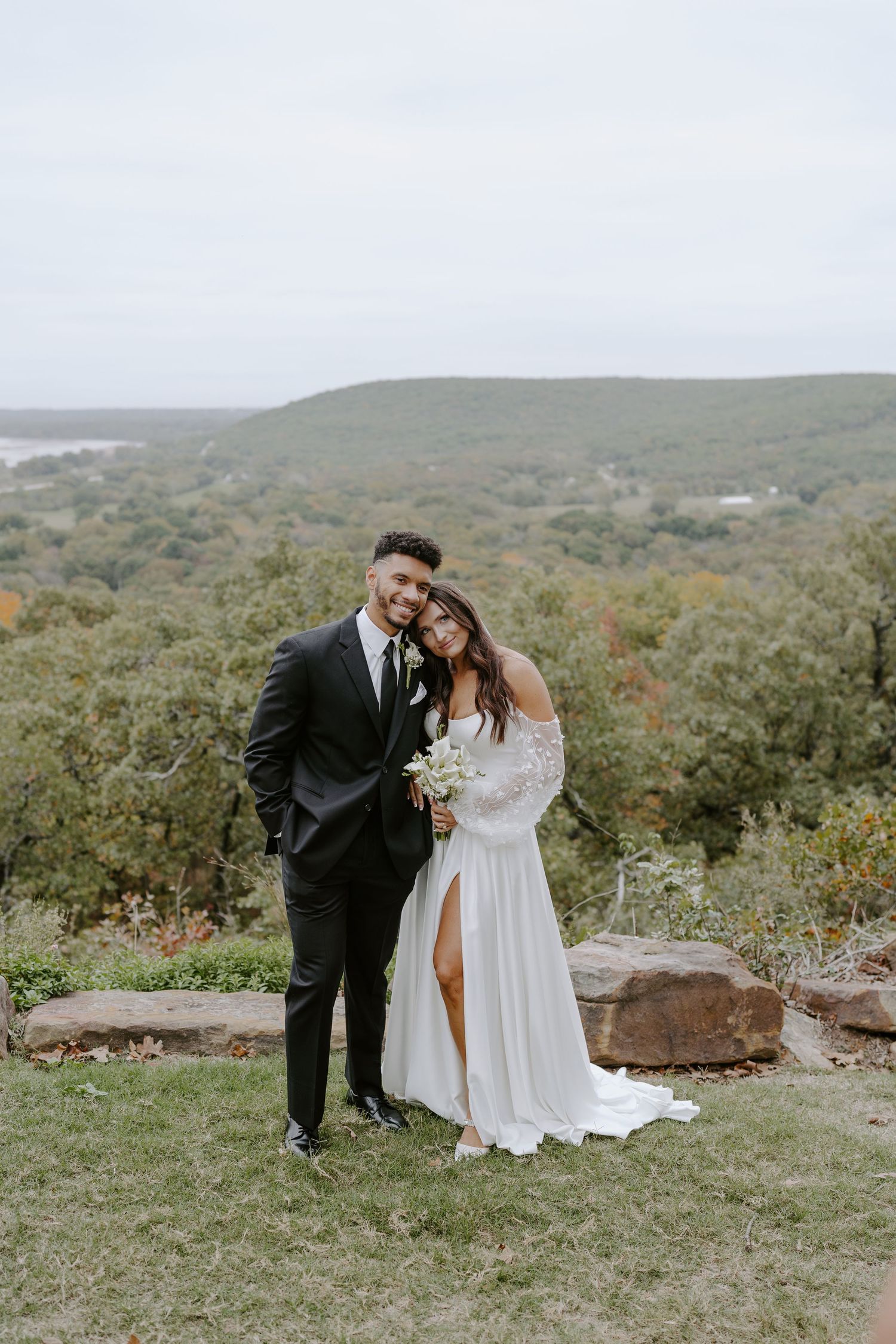 Couple shares intimate moment on scenic hilltop surrounded by autumn landscape.