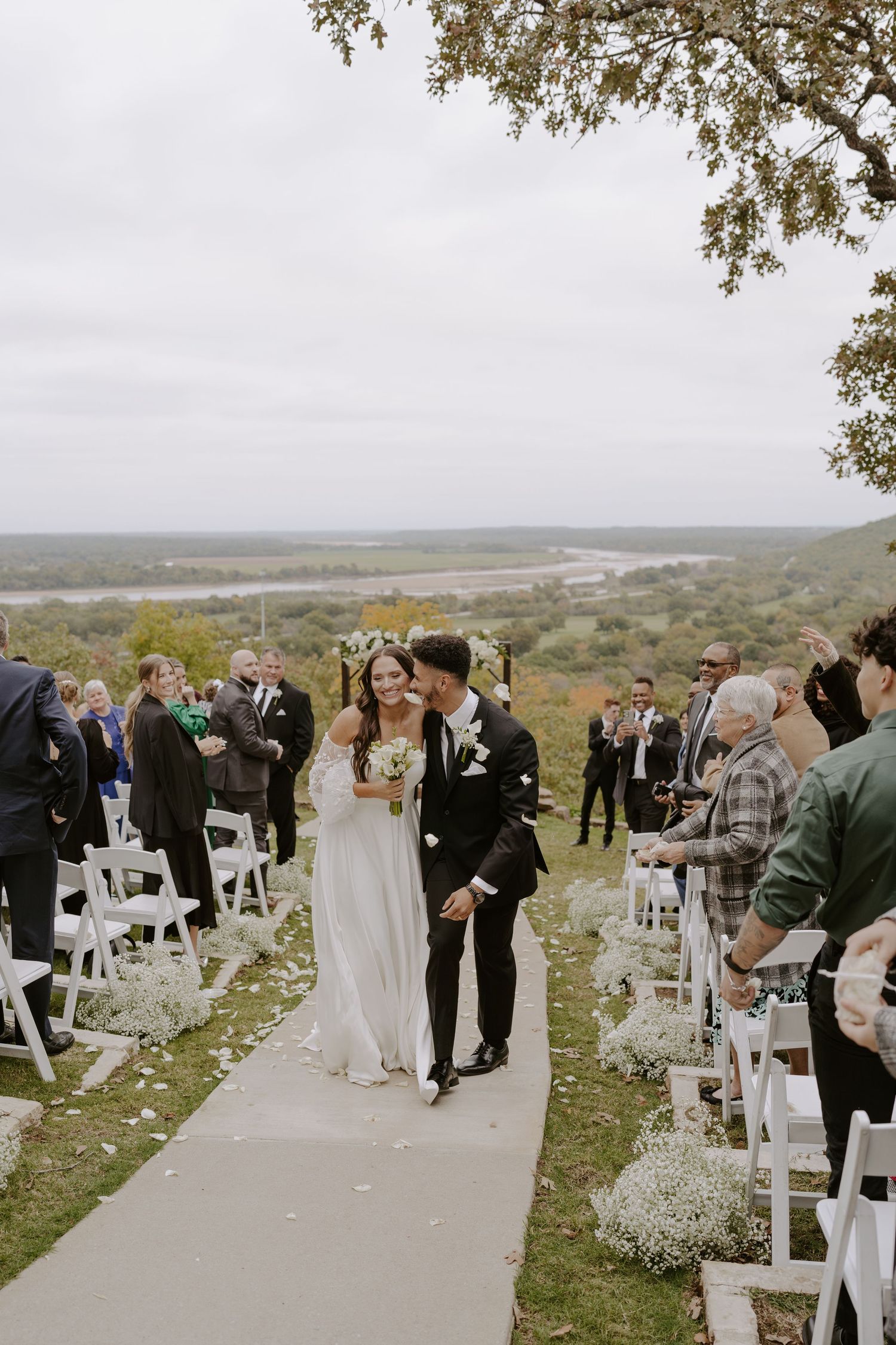 A wedding ceremony on a hillside path lined with white chairs and baby's breath flowers.