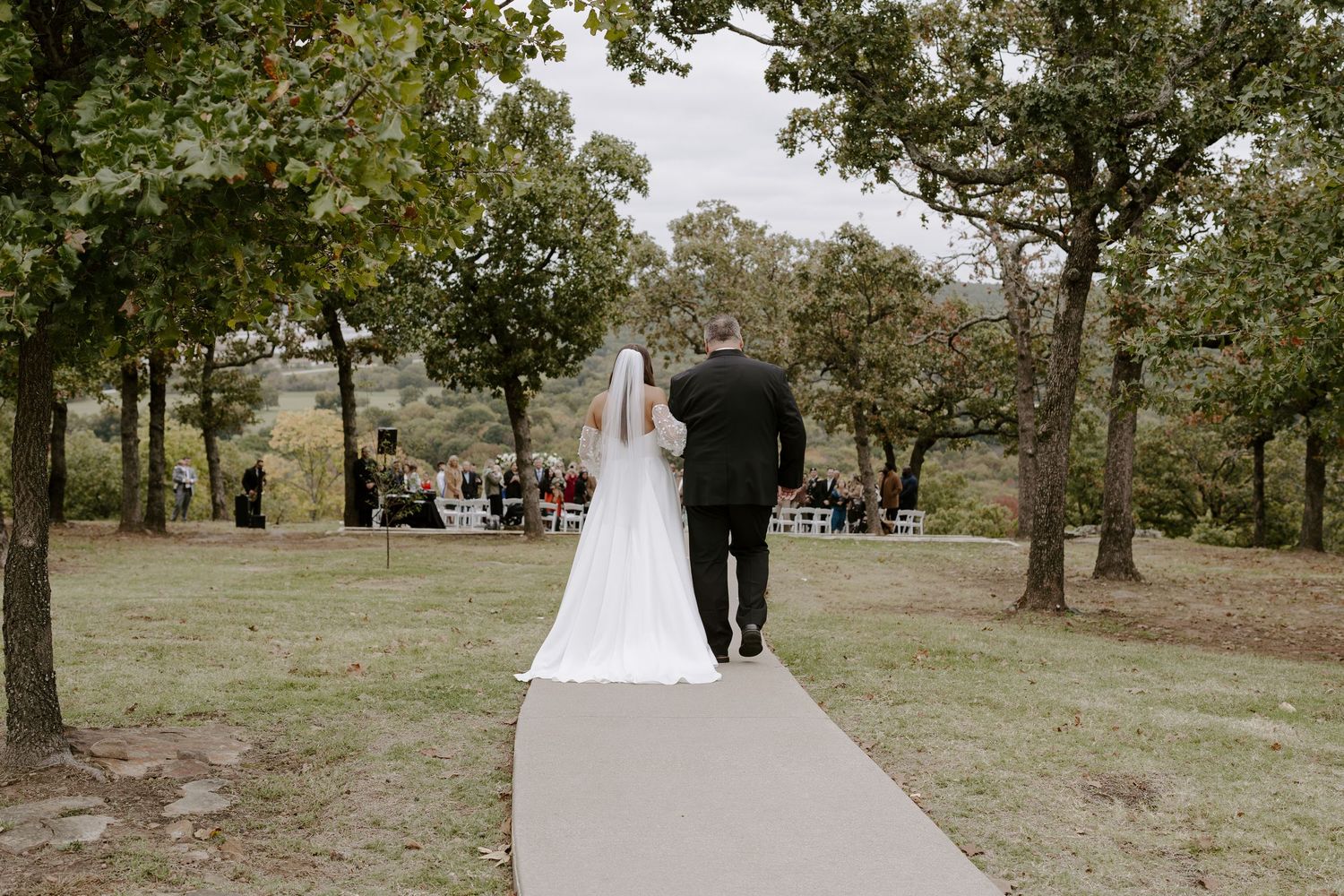 Wedding ceremony taking place on a scenic hillside with trees and natural landscaping.