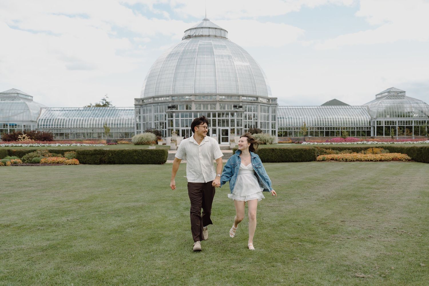 People walking across a green lawn in front of a large glass conservatory building.