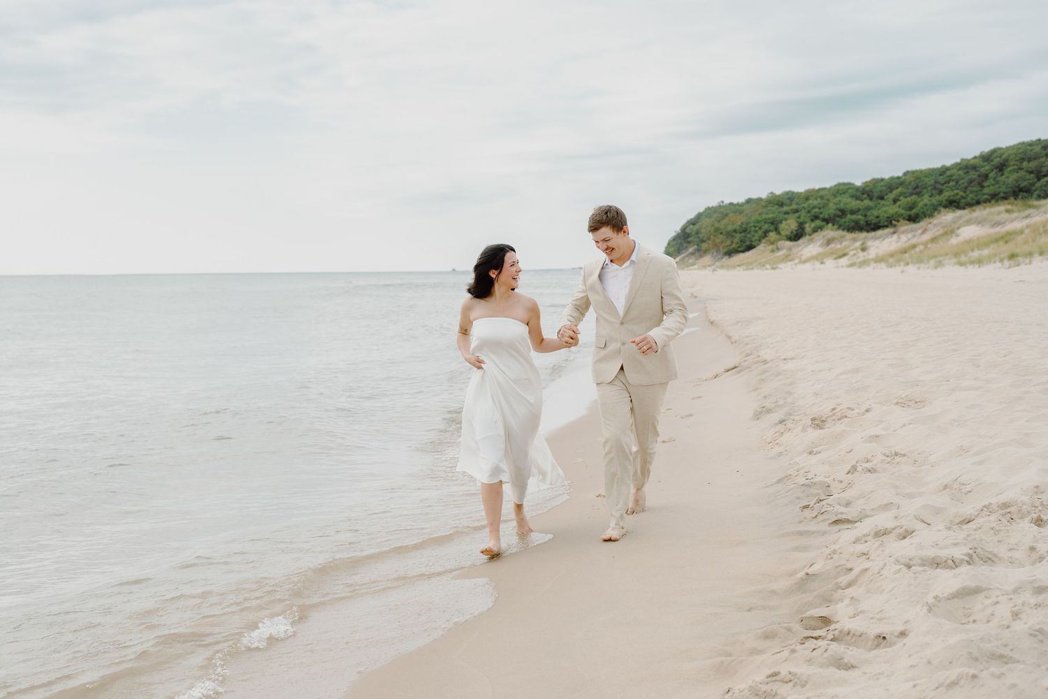 Romantic beach scene with couple walking along the water's edge near green coastal cliffs.