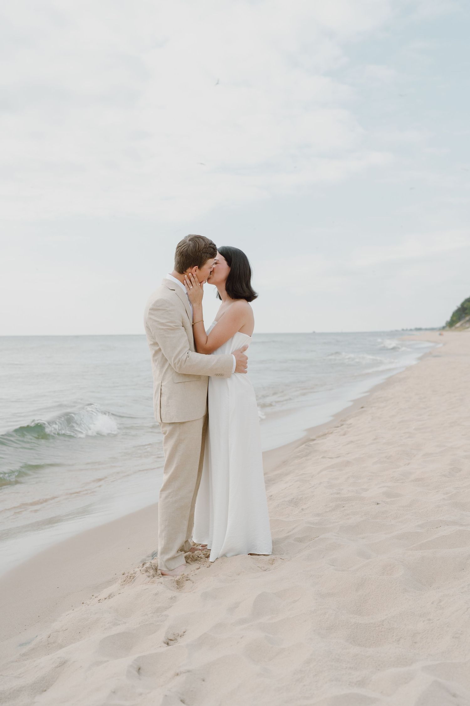 A couple in light-colored attire shares a romantic moment on a serene beach.