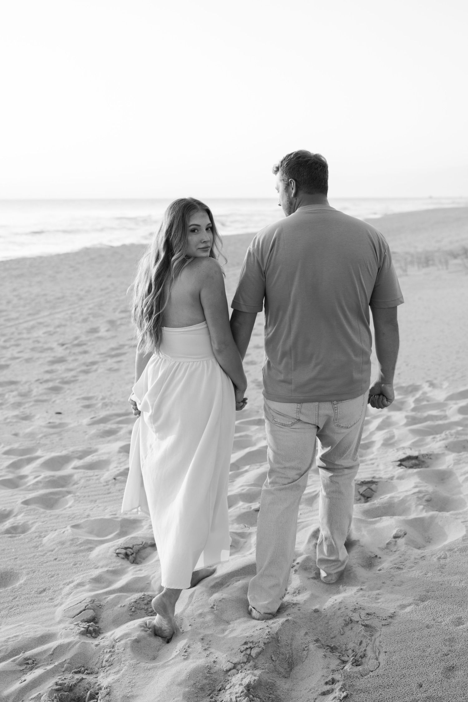 Couple walking hand in hand along a sandy beach during sunset.