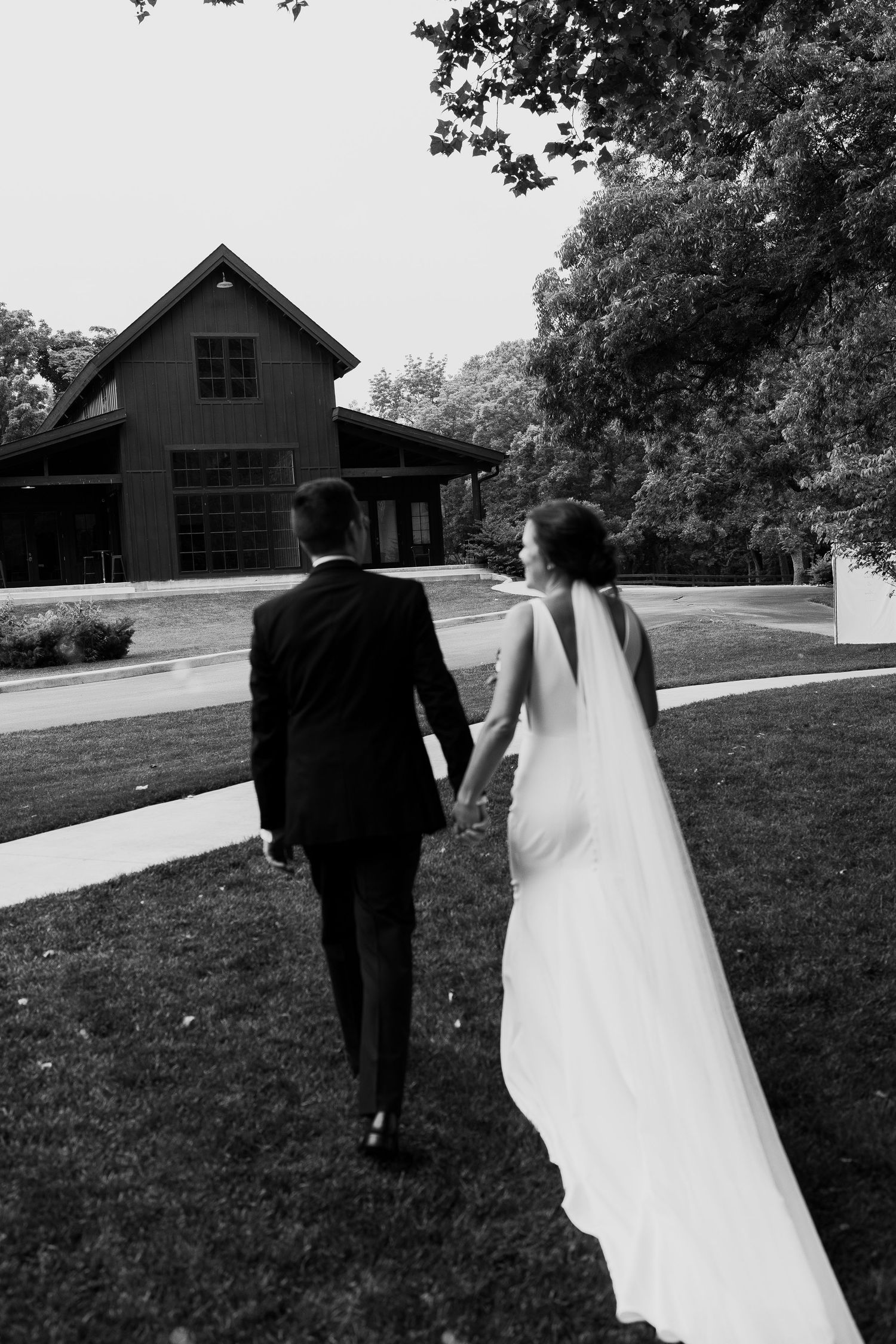 Couple walks towards a rustic barn building across a grassy lawn.