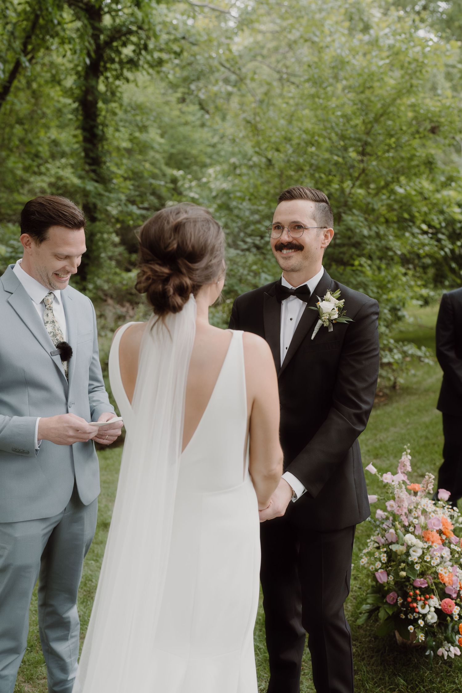 A wedding ceremony moment captured in a wooded setting with floral decorations.