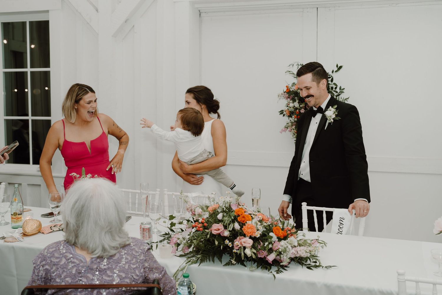 Wedding reception setup in bright white venue with floral arrangements.