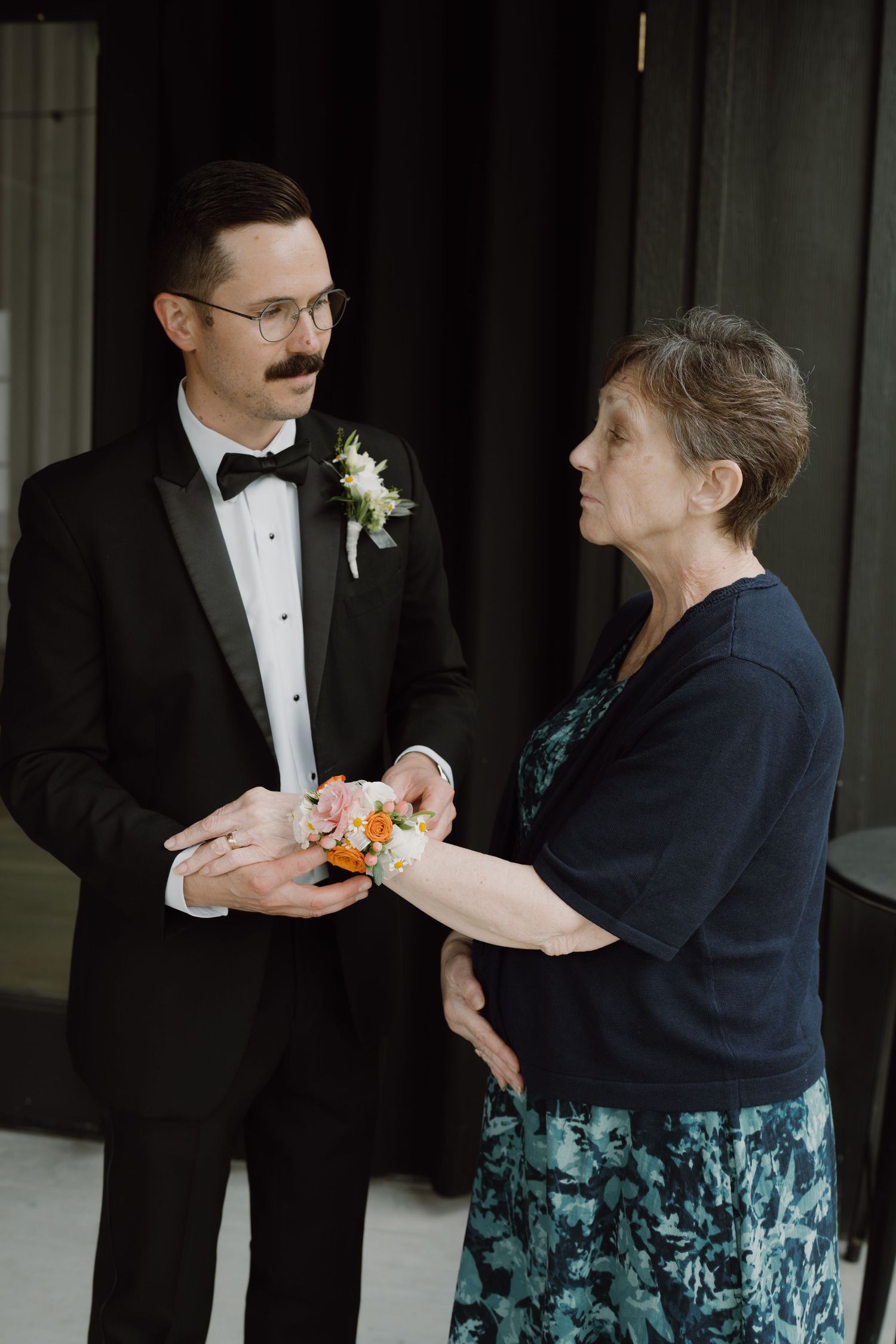Wedding party members help each other with corsages and formal attire preparations.