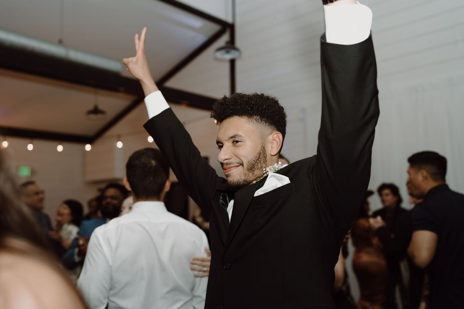 Wedding reception guests dancing and celebrating with raised arms under ambient lighting.