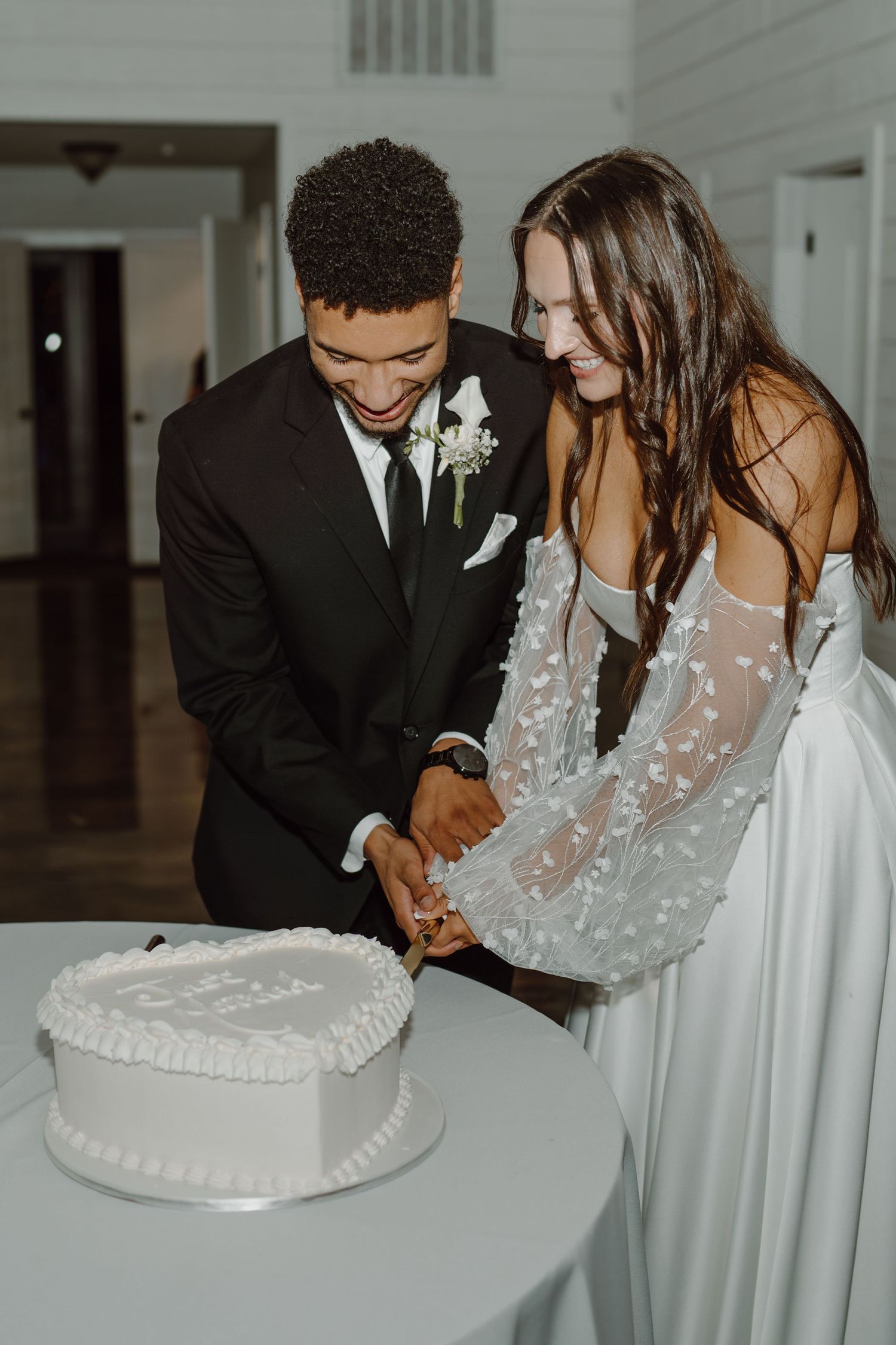 Couple cutting their white wedding cake together at the reception.