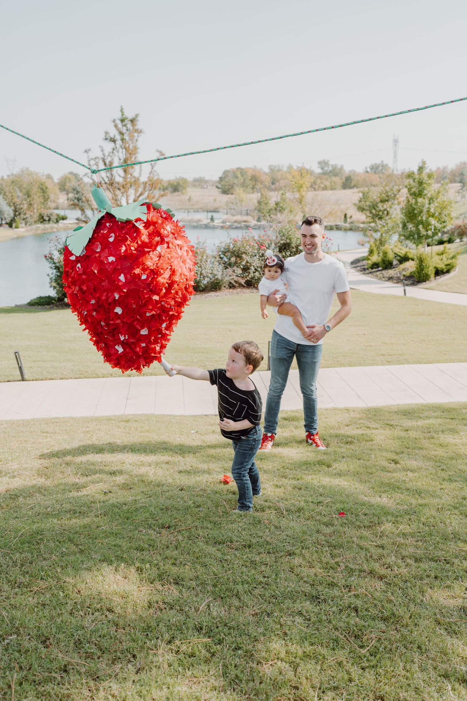 People stand on a lawn with a large red heart-shaped balloon arrangement visible in the background.