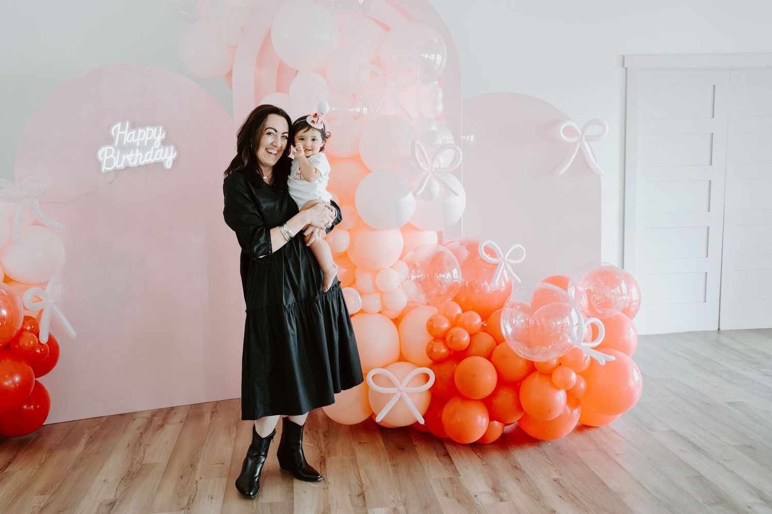 Stylish birthday photo backdrop with coral and white balloon arrangement against white wall.