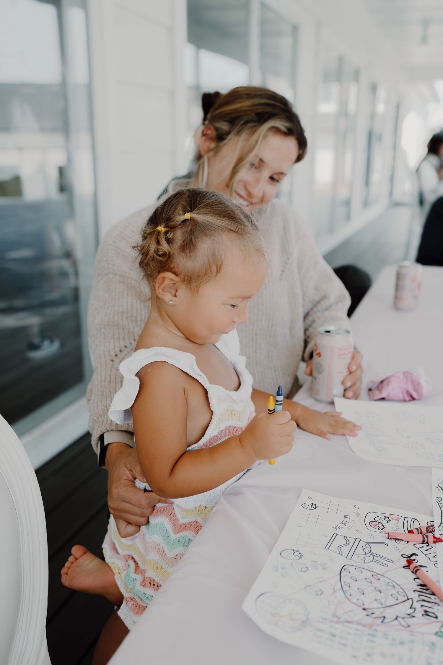 A coloring activity taking place at a white table in a bright indoor space.