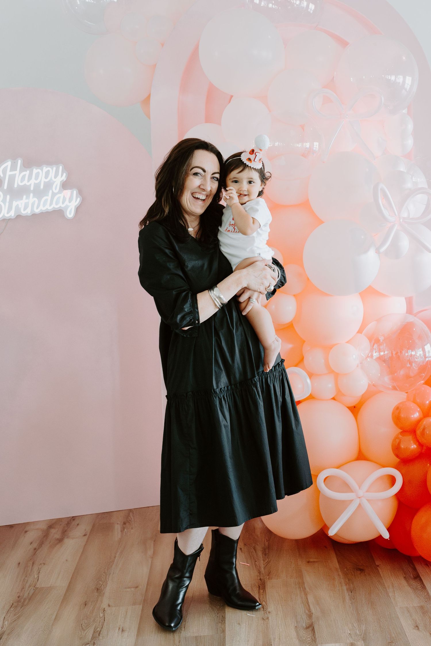 Black and coral themed birthday photoshoot setup with balloon garland and wooden floor.