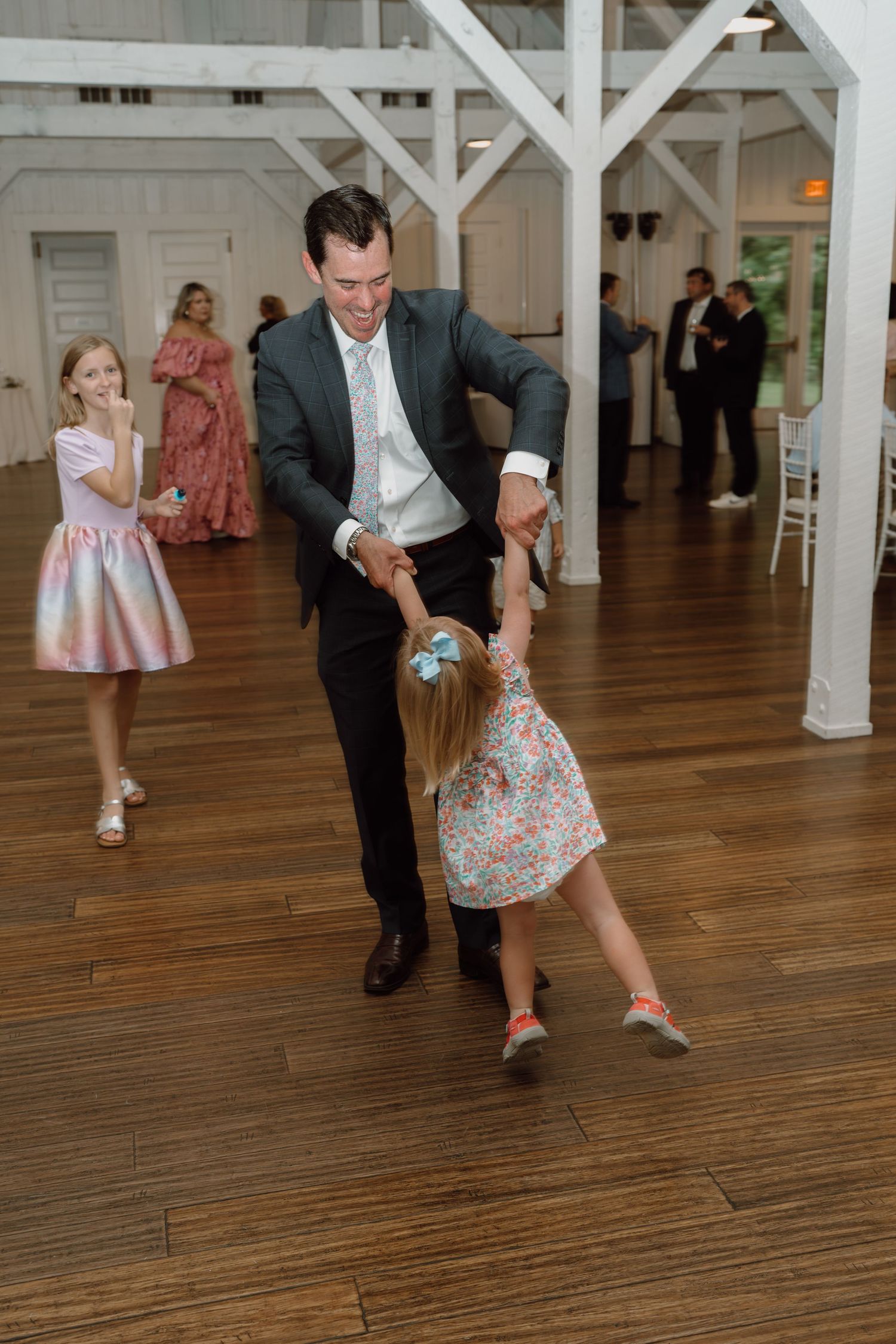 Playful dancing moments captured on the wooden floor of a wedding venue.