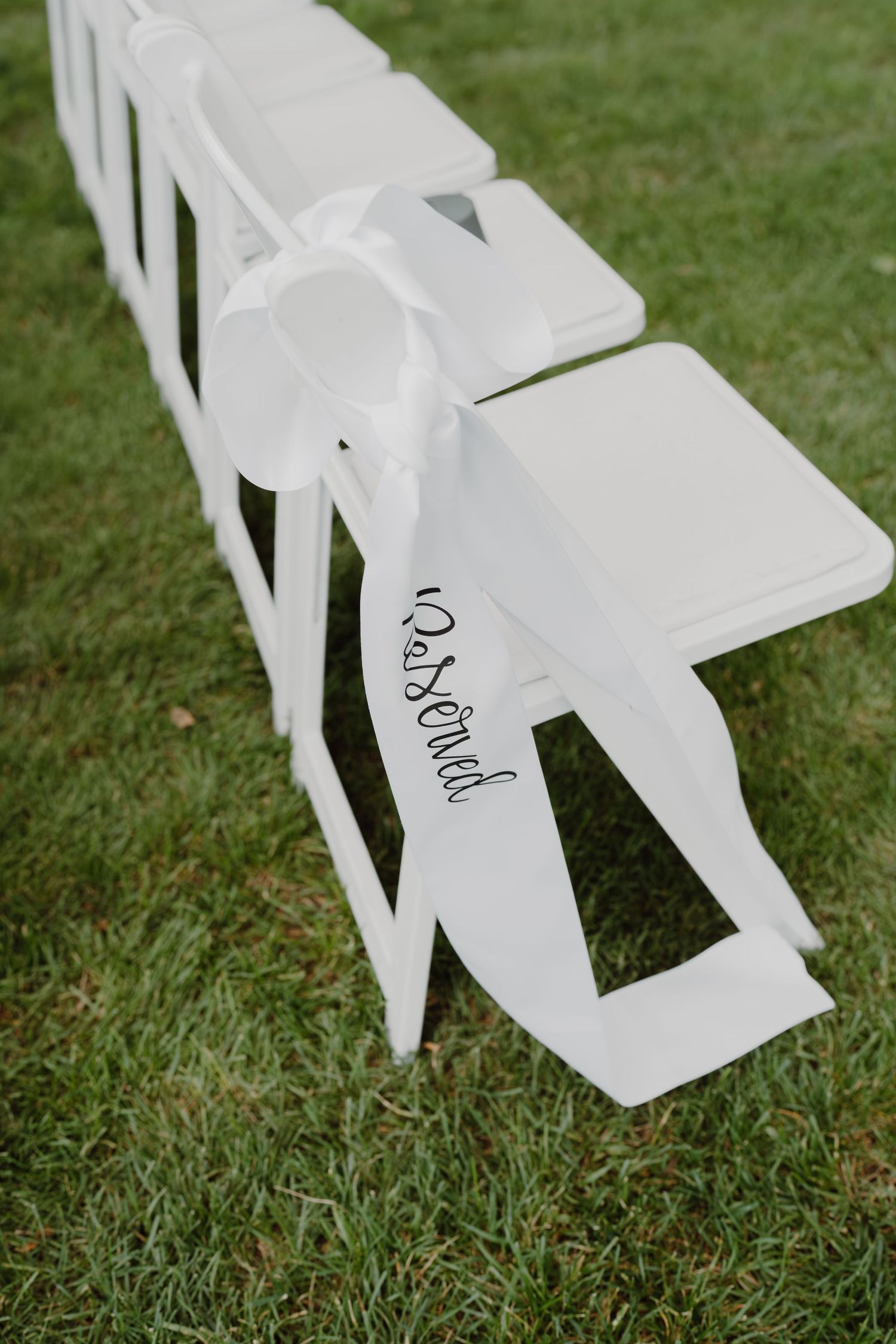 White folding chairs with handwritten text set up on green grass.