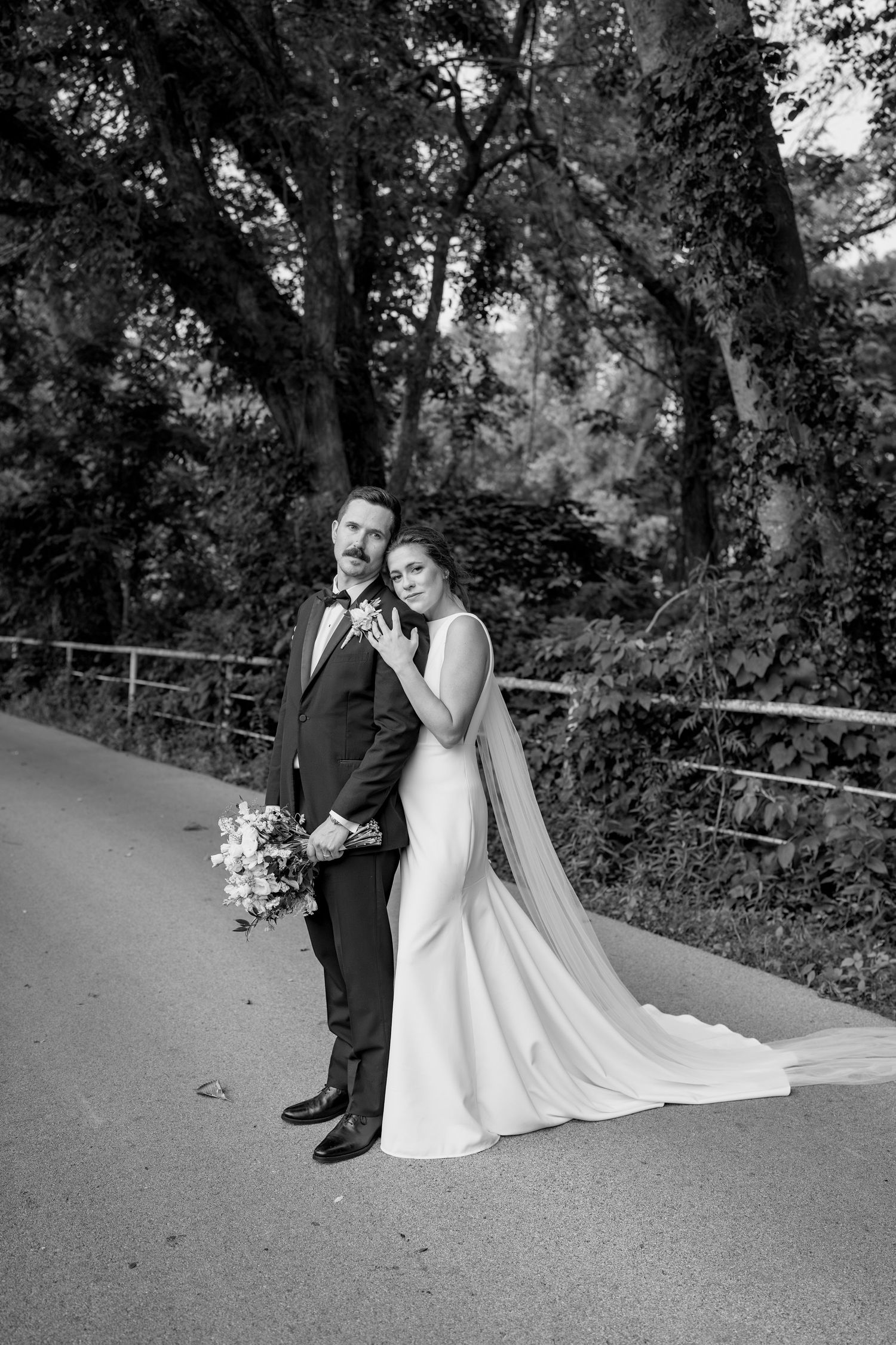 Black and white wedding portrait on pathway with elegant dress and natural backdrop.