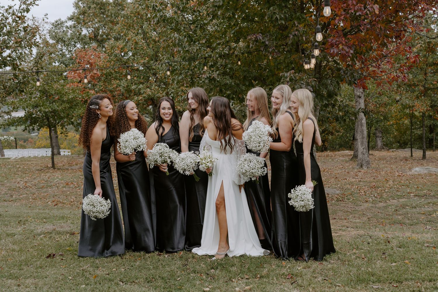A wedding party poses outdoors during autumn with colorful fall foliage in the background.