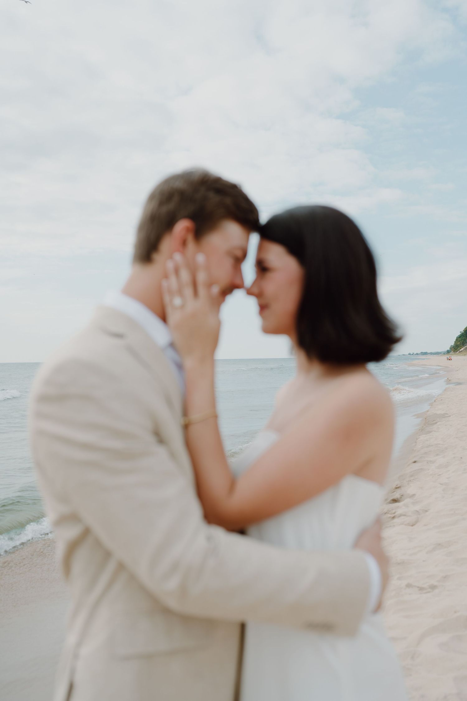 A tender moment captured between a couple in wedding attire on a sunny beach.