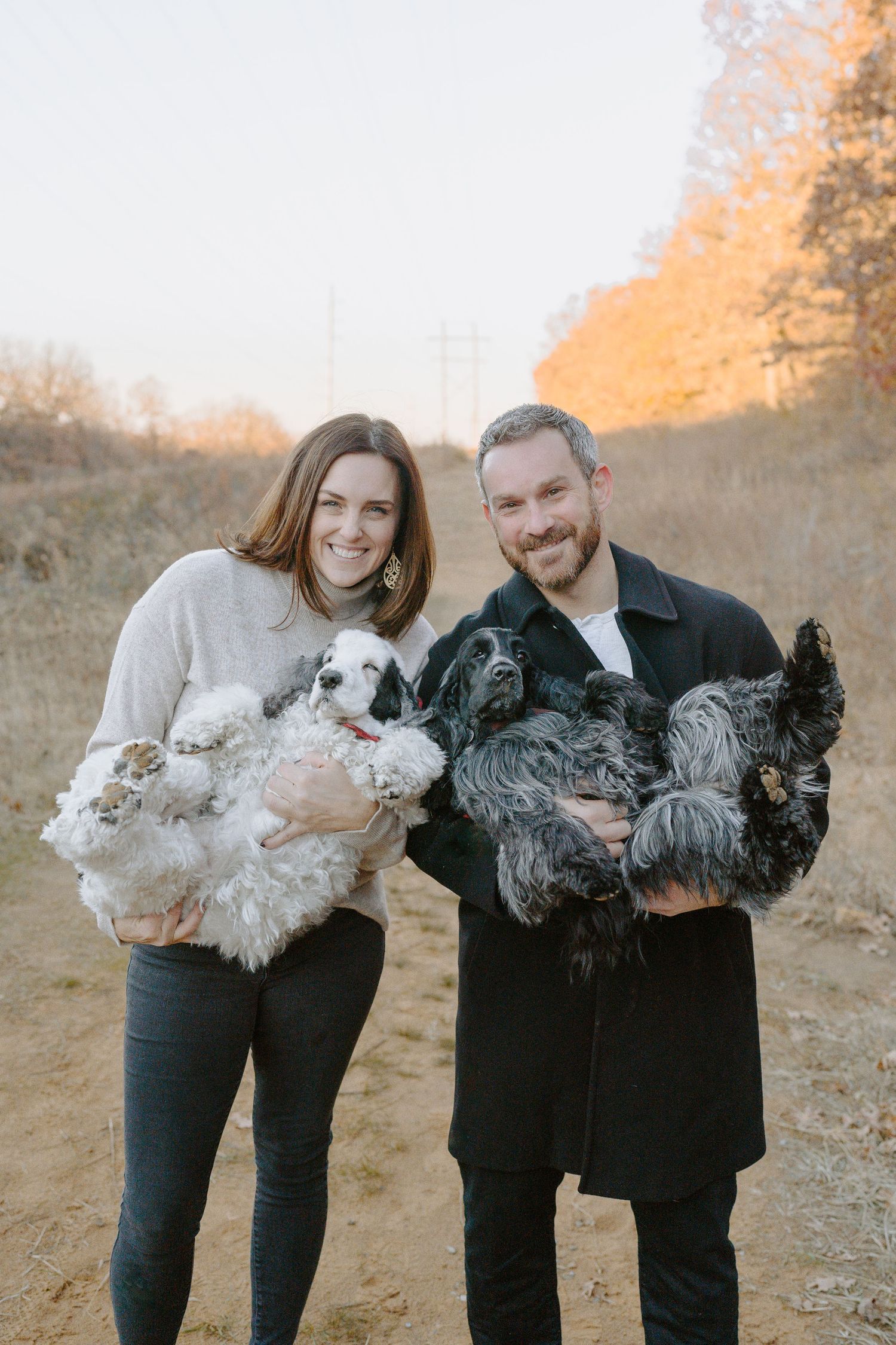A couple poses outdoors holding fluffy chickens against an autumn backdrop.