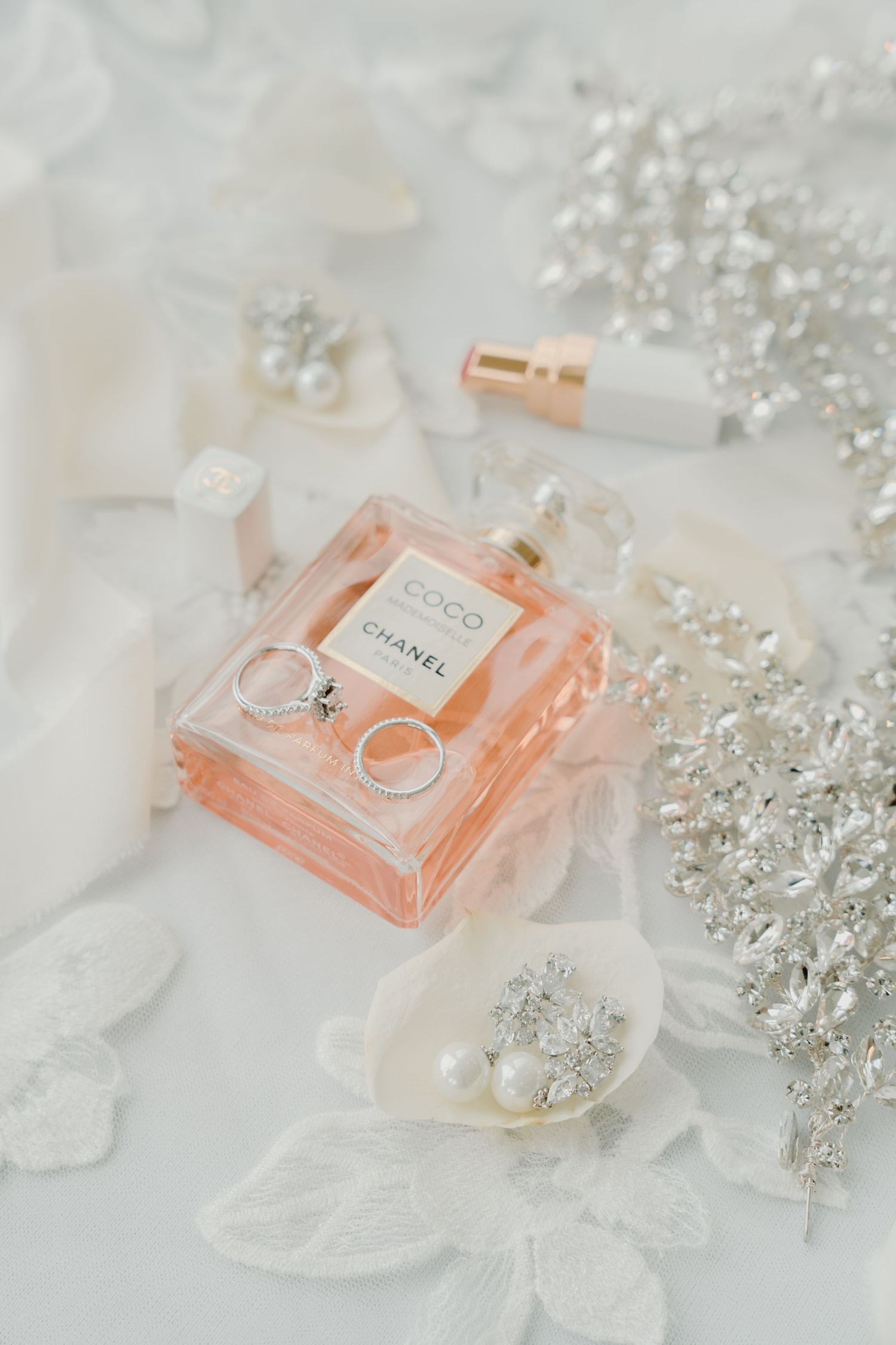 Elegant perfume bottle in peach color surrounded by crystal accessories on white lace.