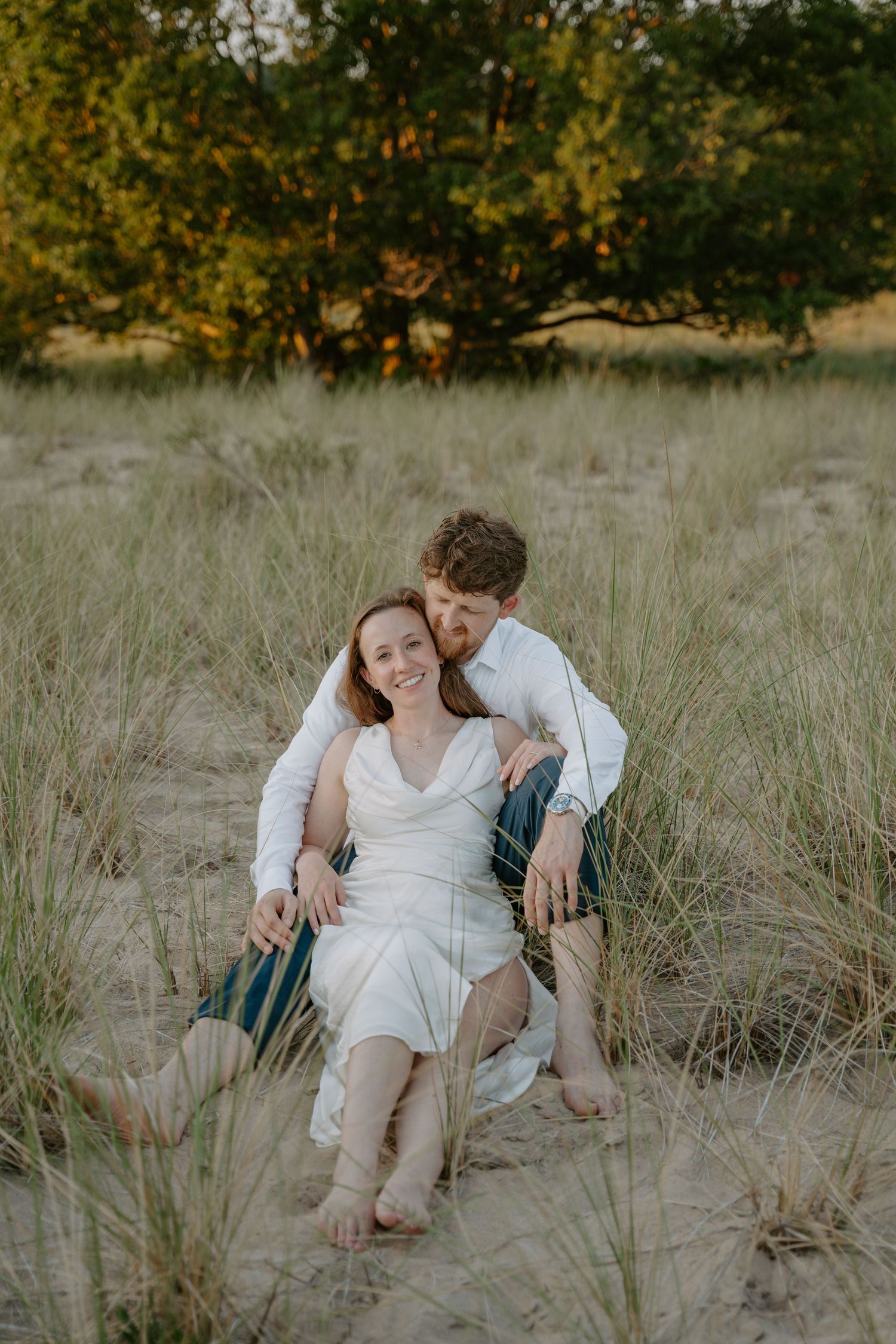 A couple shares an intimate moment while sitting in tall grass during golden hour.
