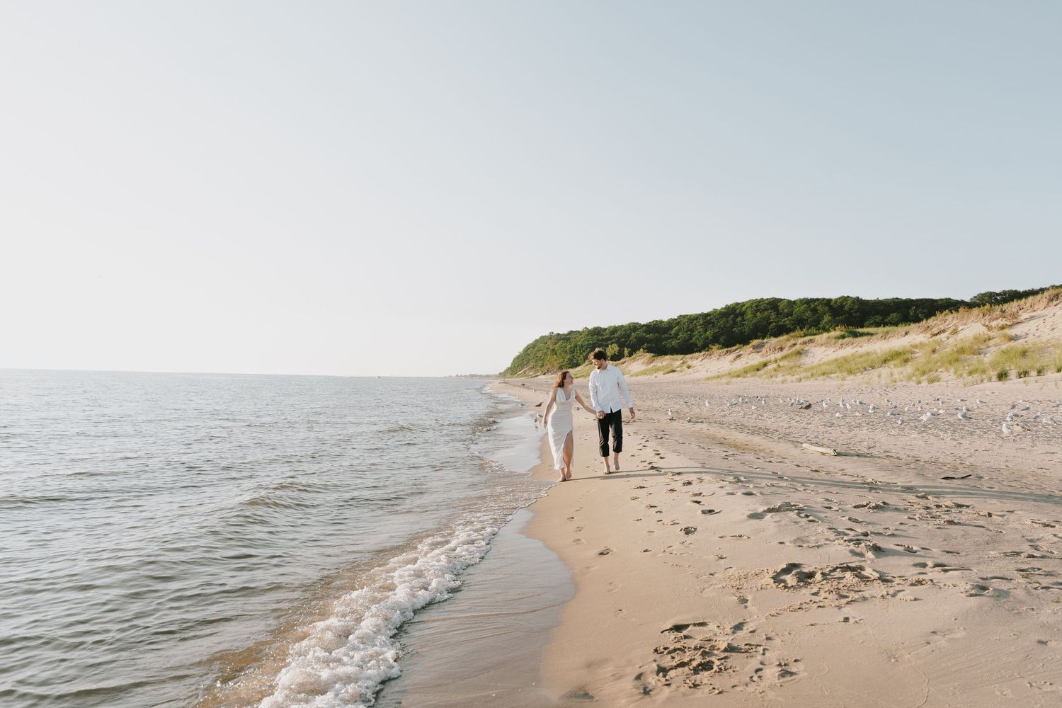 Distant view of a couple walking along a peaceful beach with cliffs in the background.