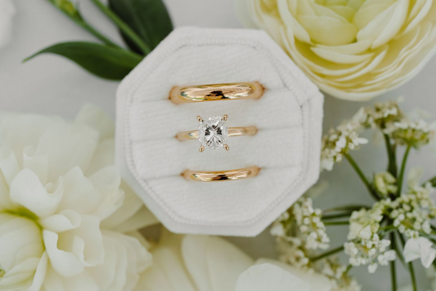 Gold wedding bands displayed with white roses and delicate greenery.