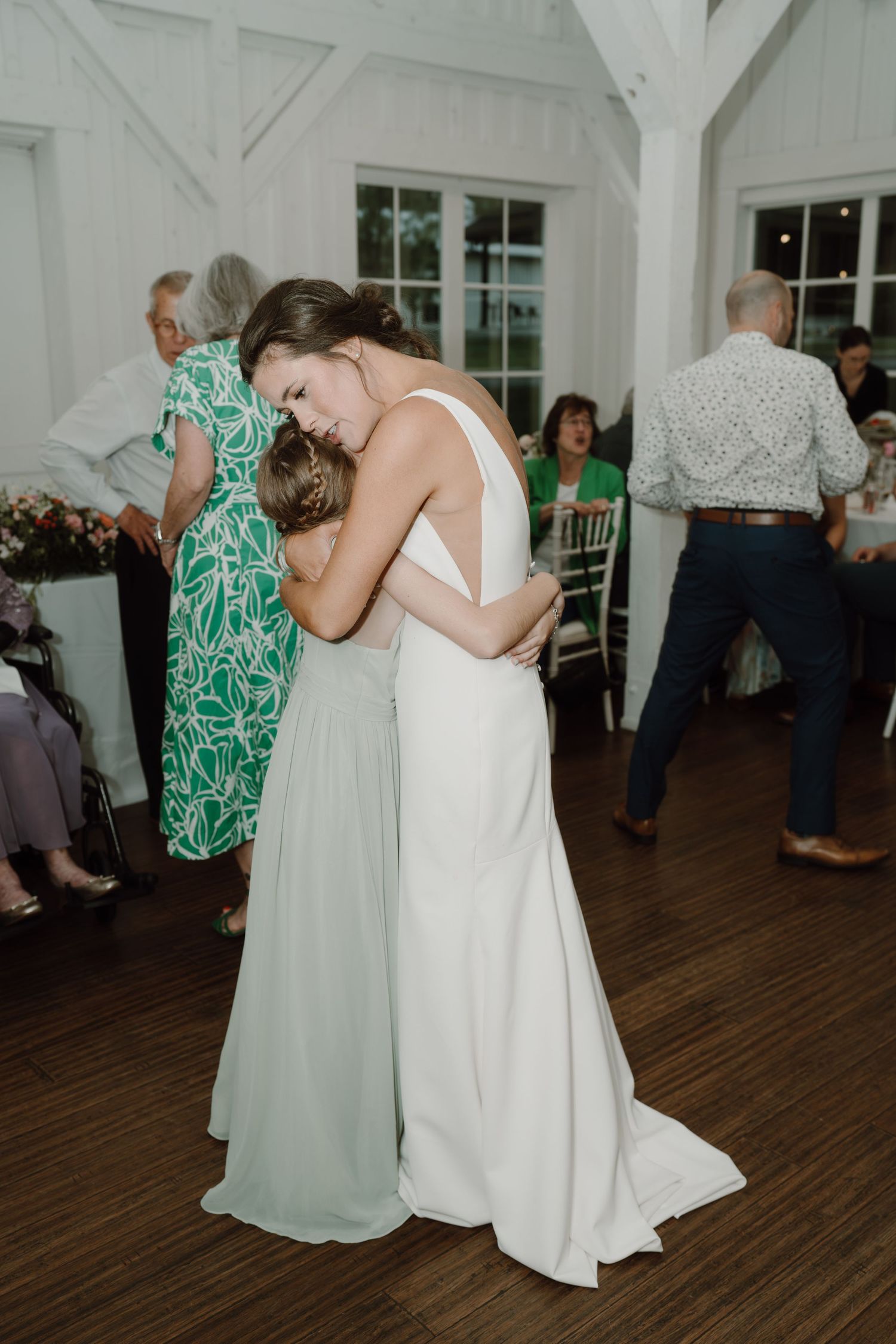 Wedding guests dancing together in a white reception hall with wooden floors.