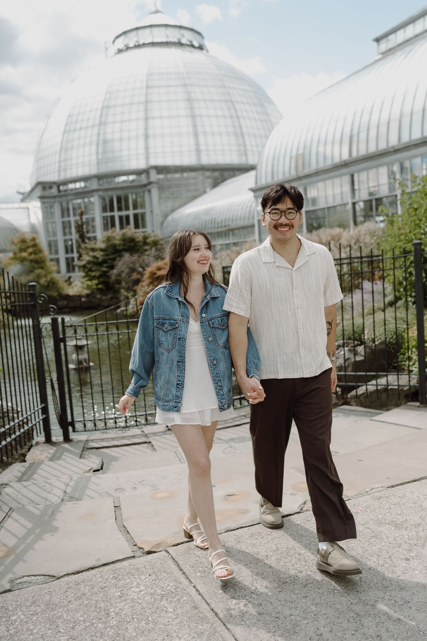 Couple walking together on stone pathway with large glass dome conservatory in background.