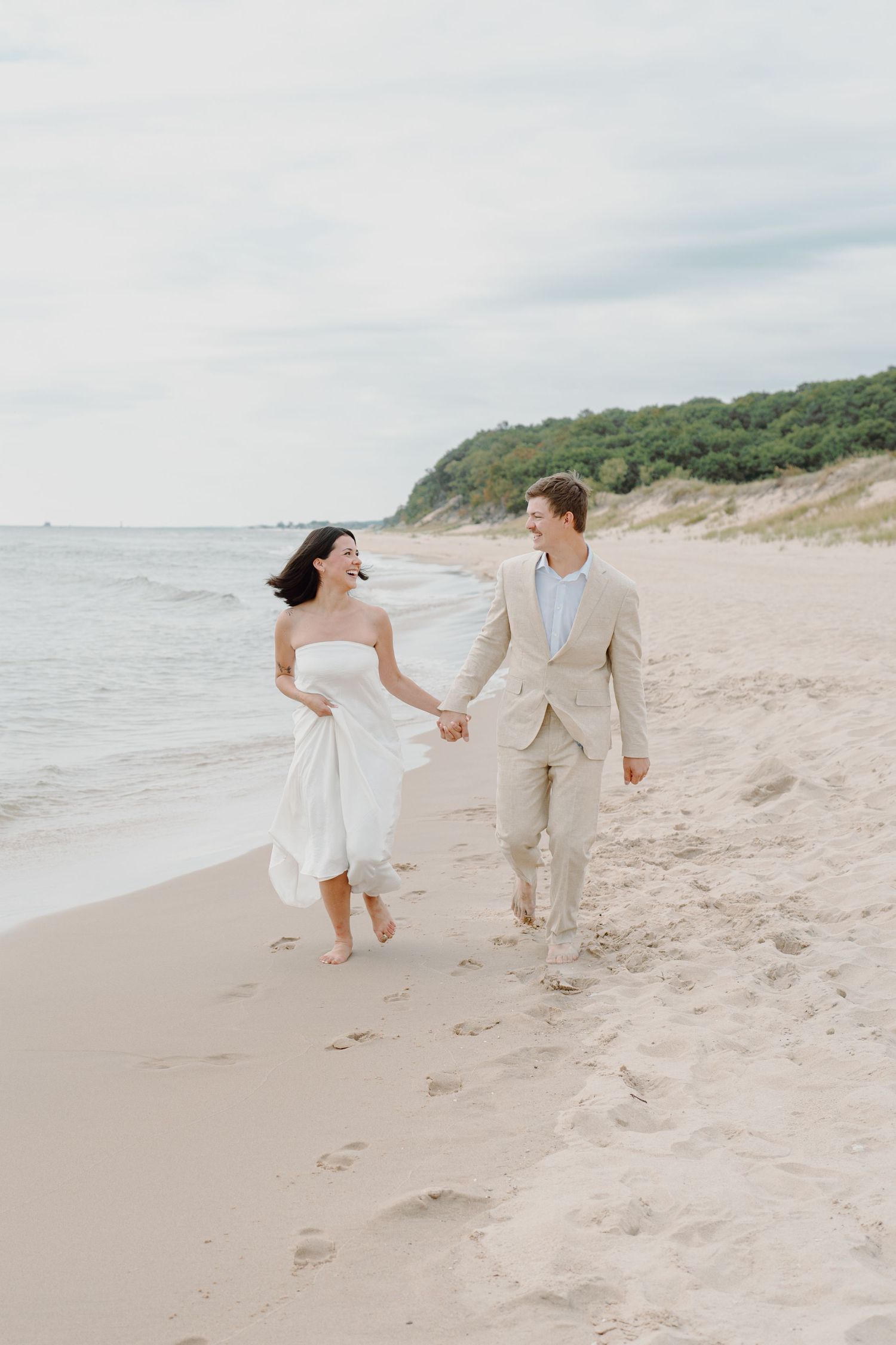A couple holds hands while running playfully along the shoreline of a scenic beach.