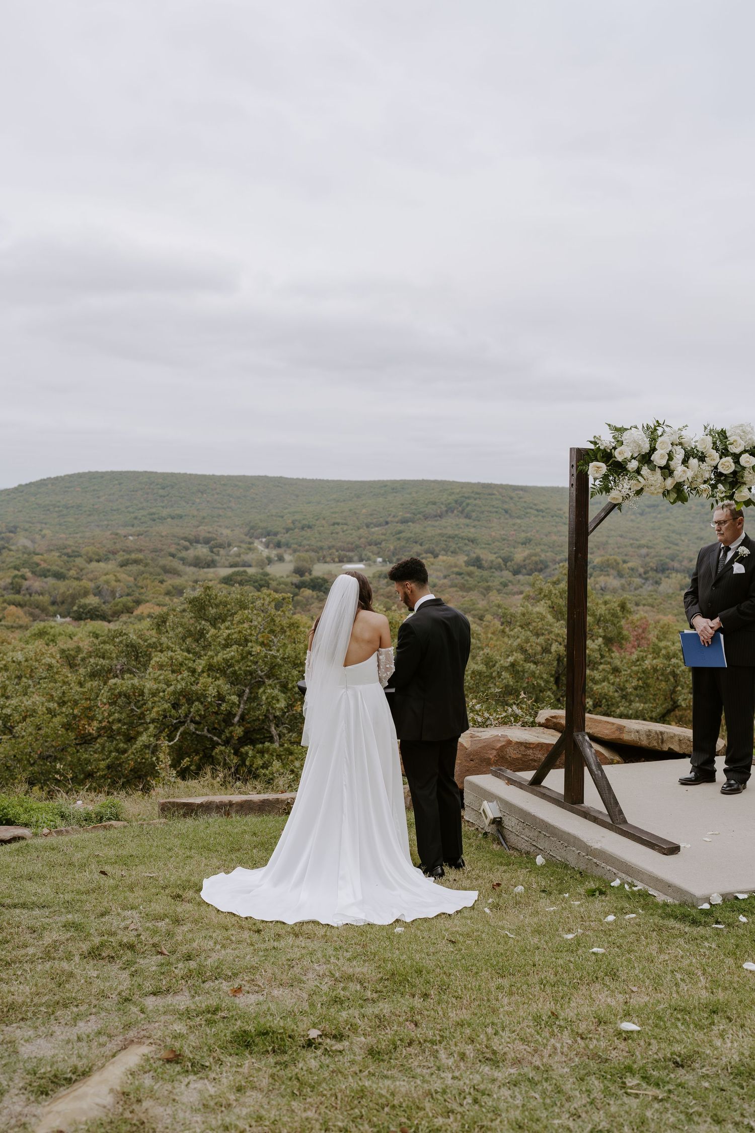 Wedding ceremony on hilltop overlook with wooden arch and mountain vista in background.